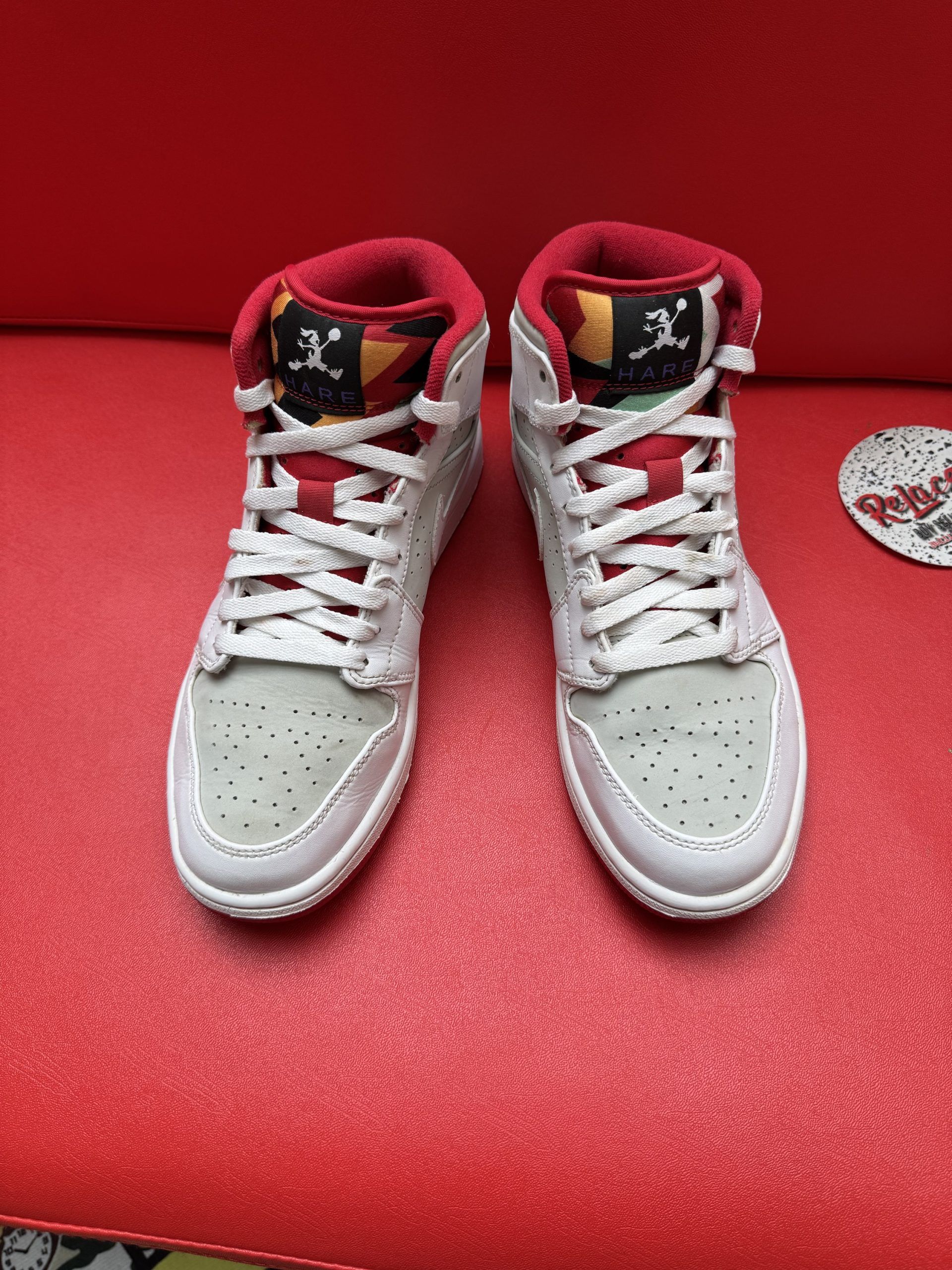 Light grey and white Air Jordan shoe with red accents, sole up, on a red surface.