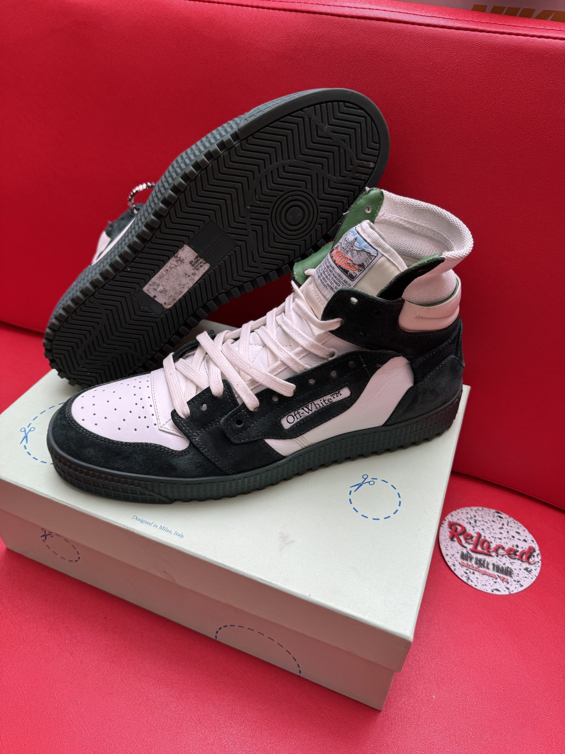 Off-White high-top sneakers in white and black, on a box, sole up. Black sole, red background.