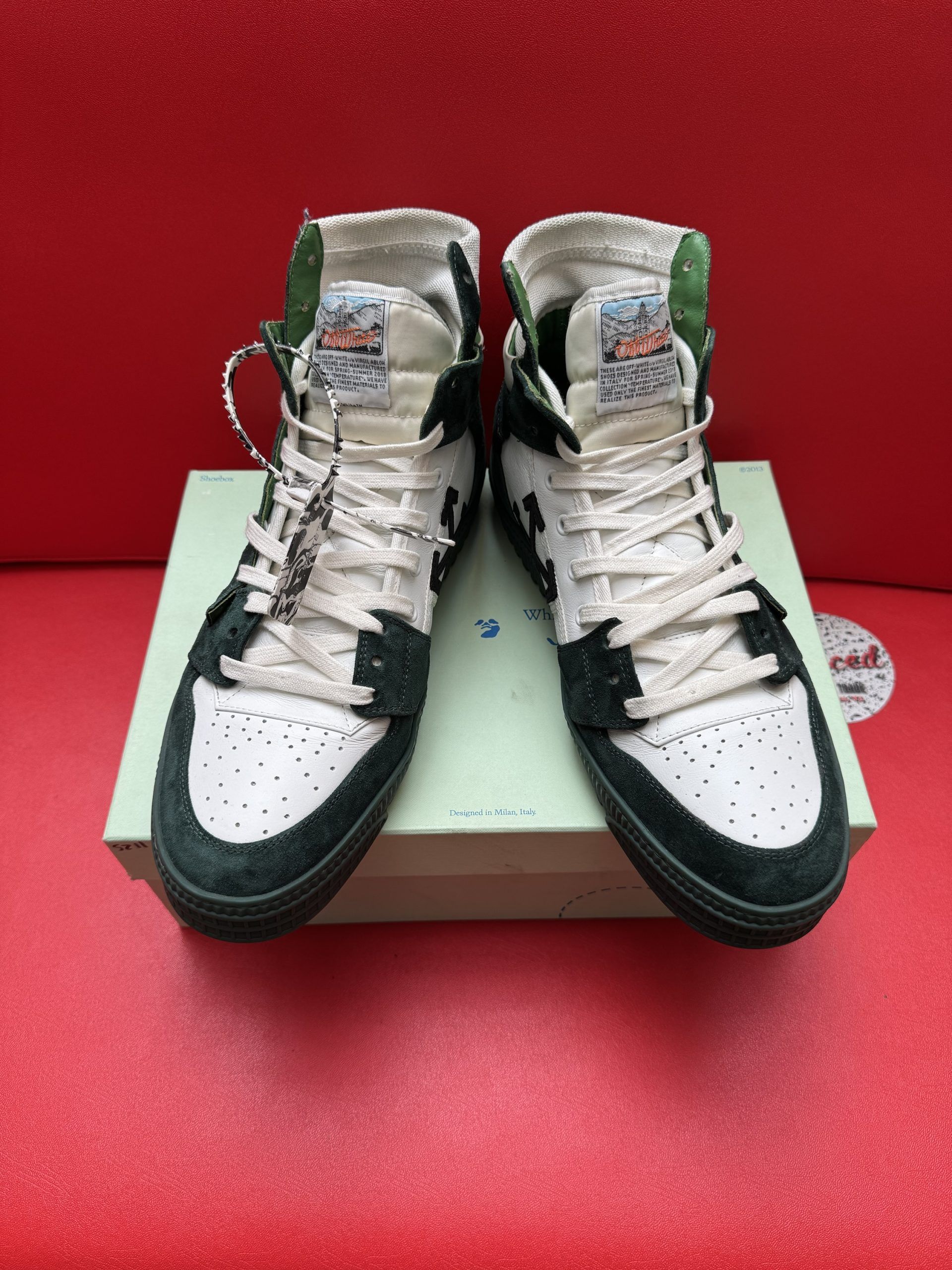 Off-White high-top sneakers in white and black, on a box, sole up. Black sole, red background.