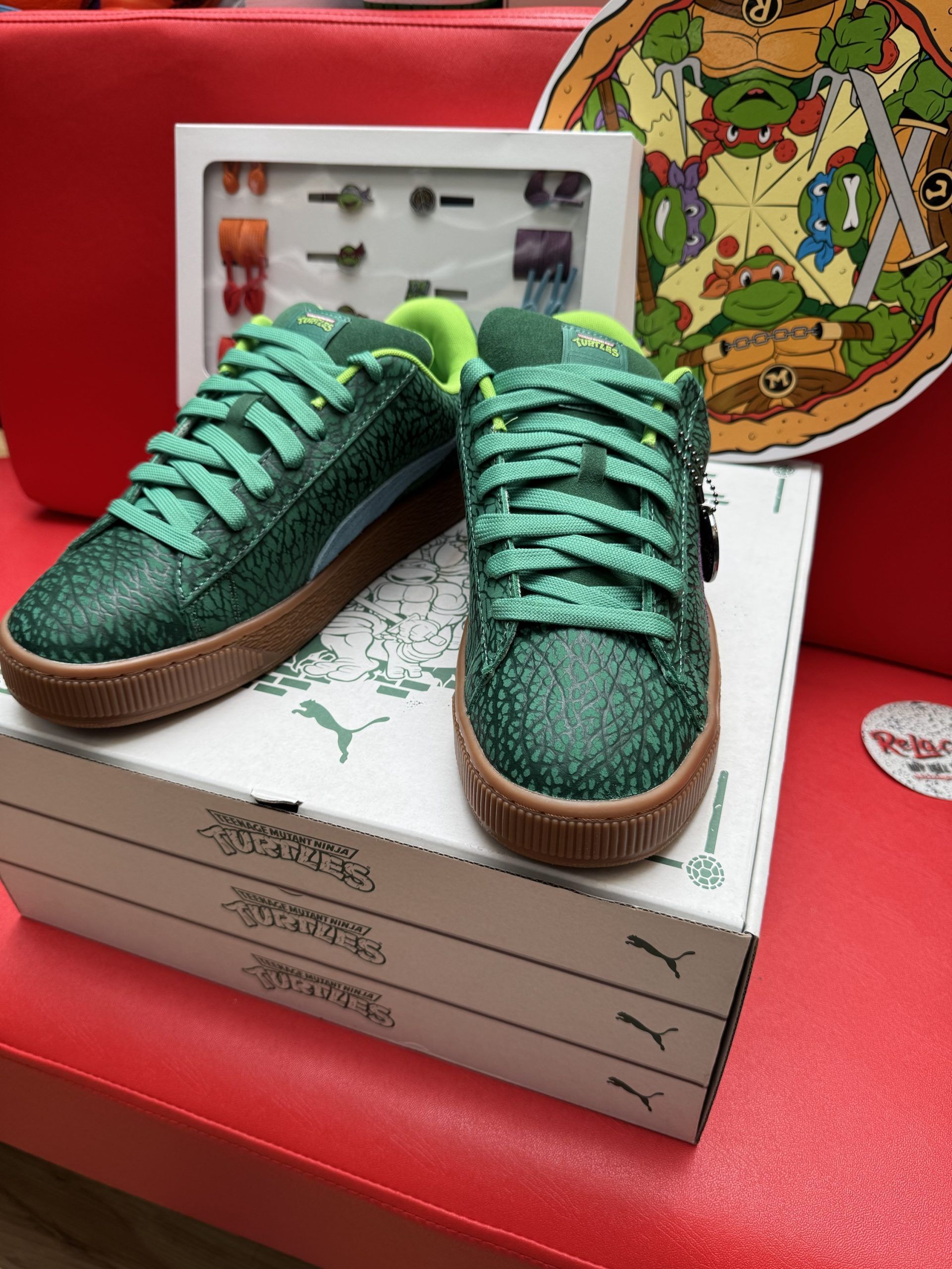 Green and purple Puma sneakers with Teenage Mutant Ninja Turtles theme, on pizza box.