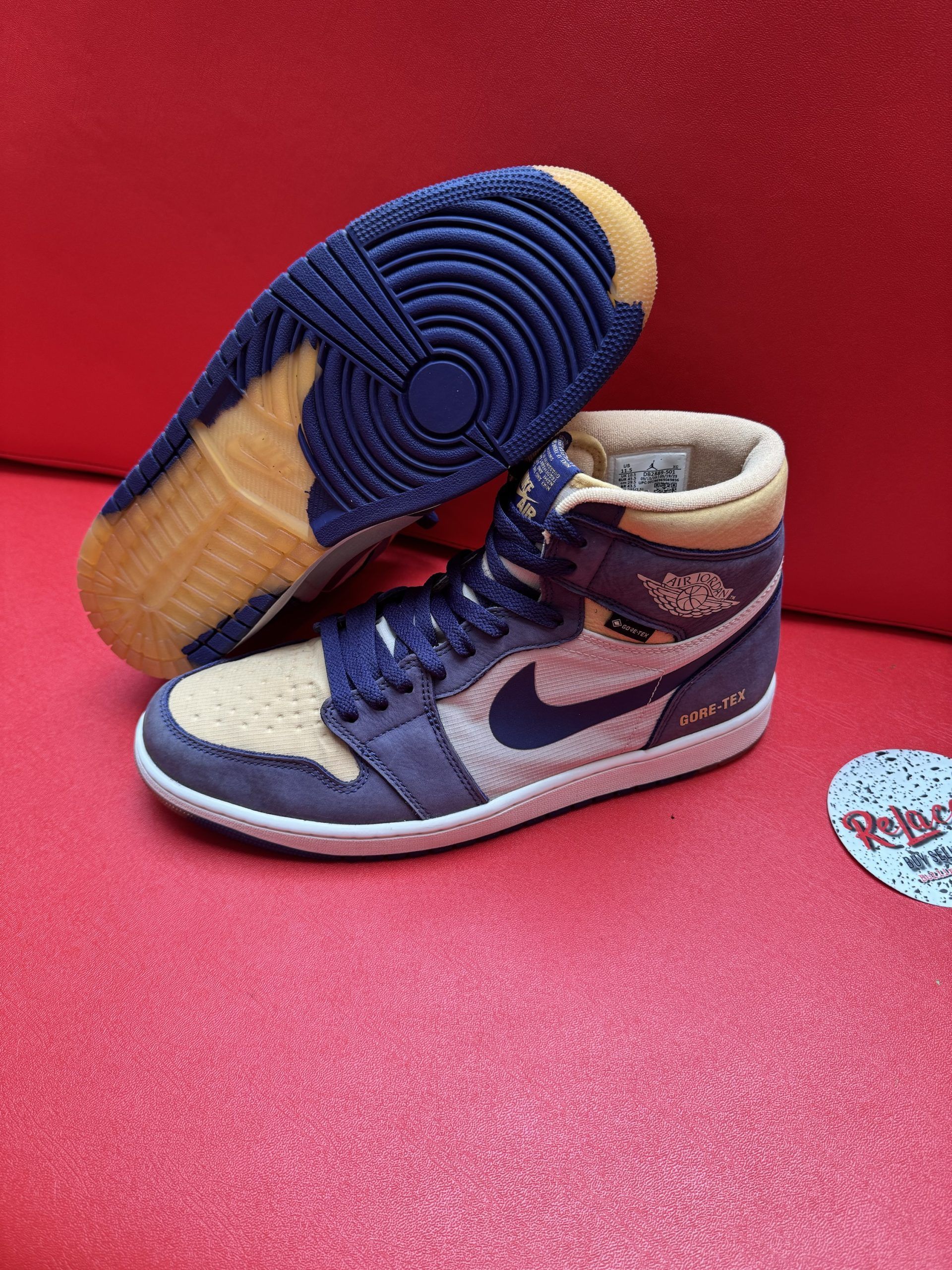 Air Jordan 1 sneaker, tan and navy blue, sitting on a red surface, sole facing up.