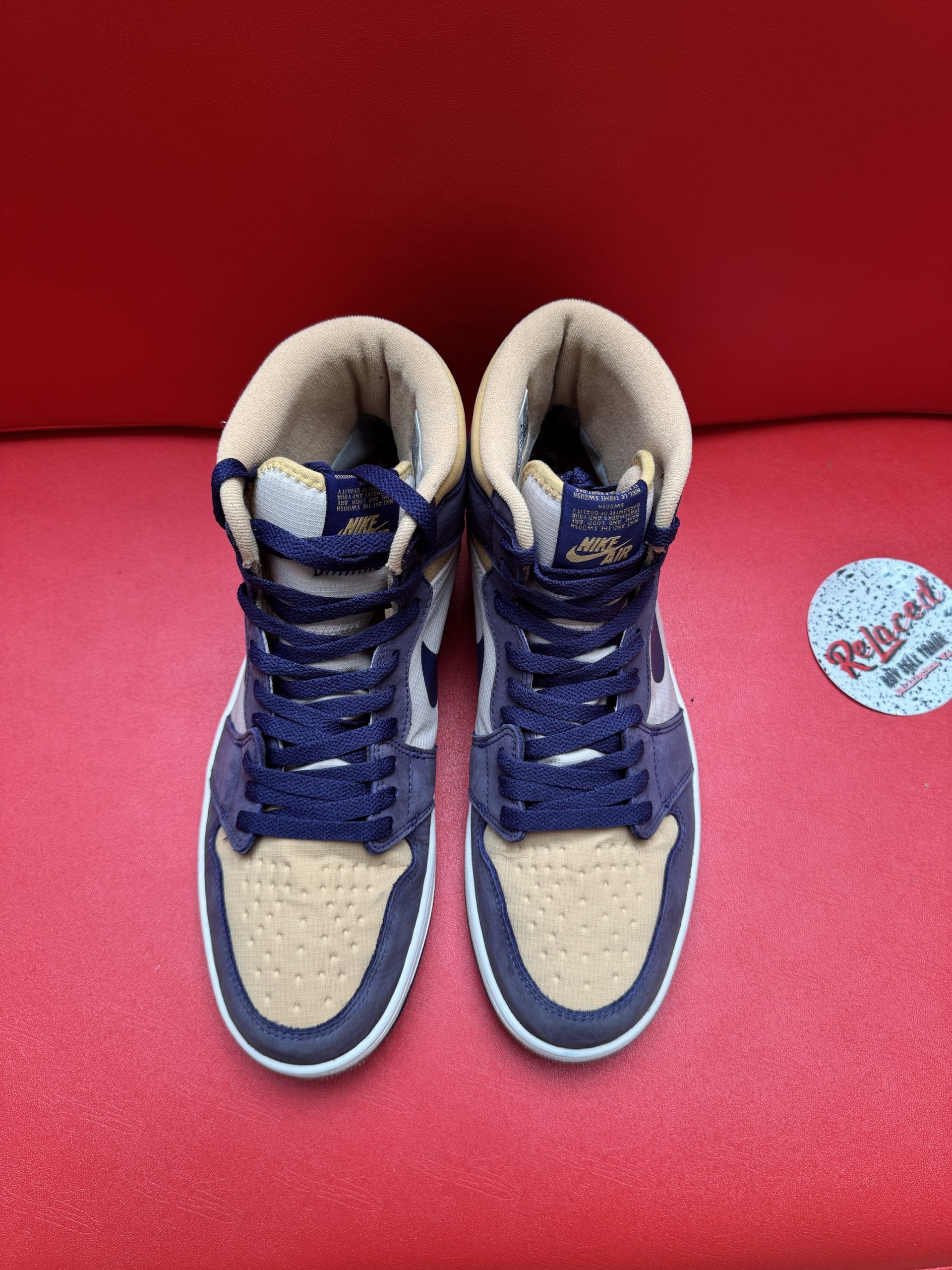 Air Jordan 1 sneaker, tan and navy blue, sitting on a red surface, sole facing up.