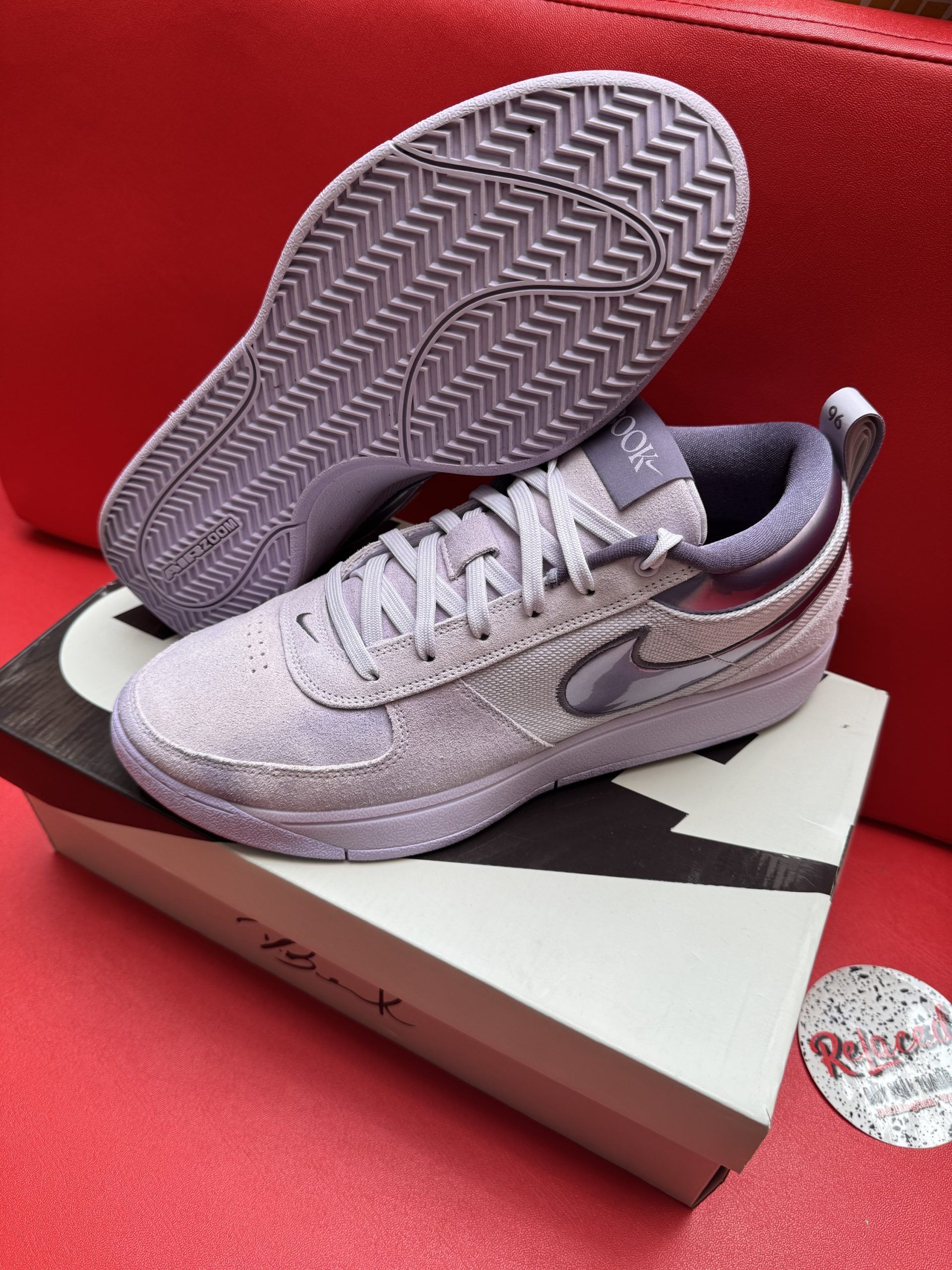 Purple Nike sneakers on a box, with a textured sole, set on a red surface.