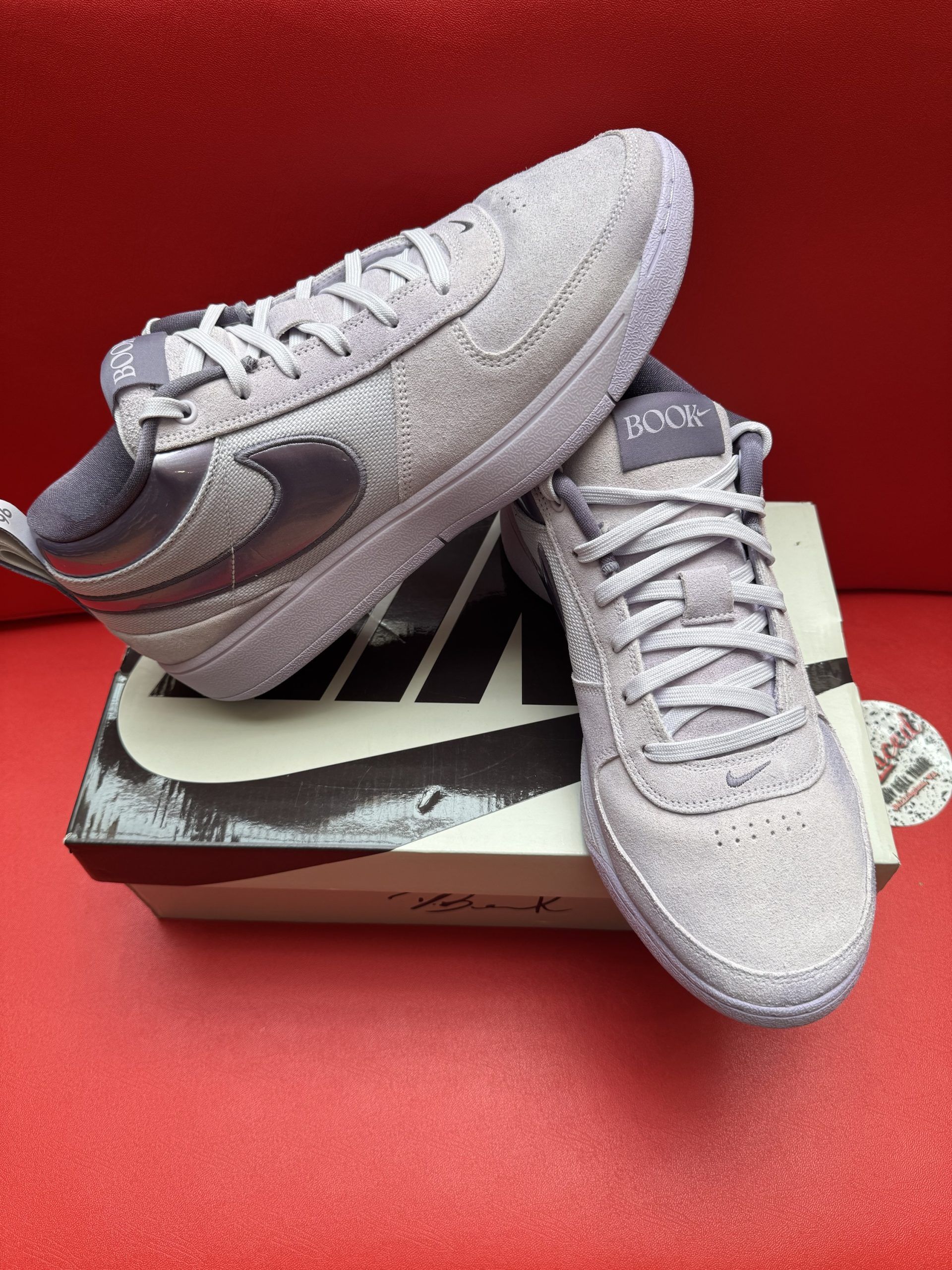 Purple Nike sneakers on a box, with a textured sole, set on a red surface.