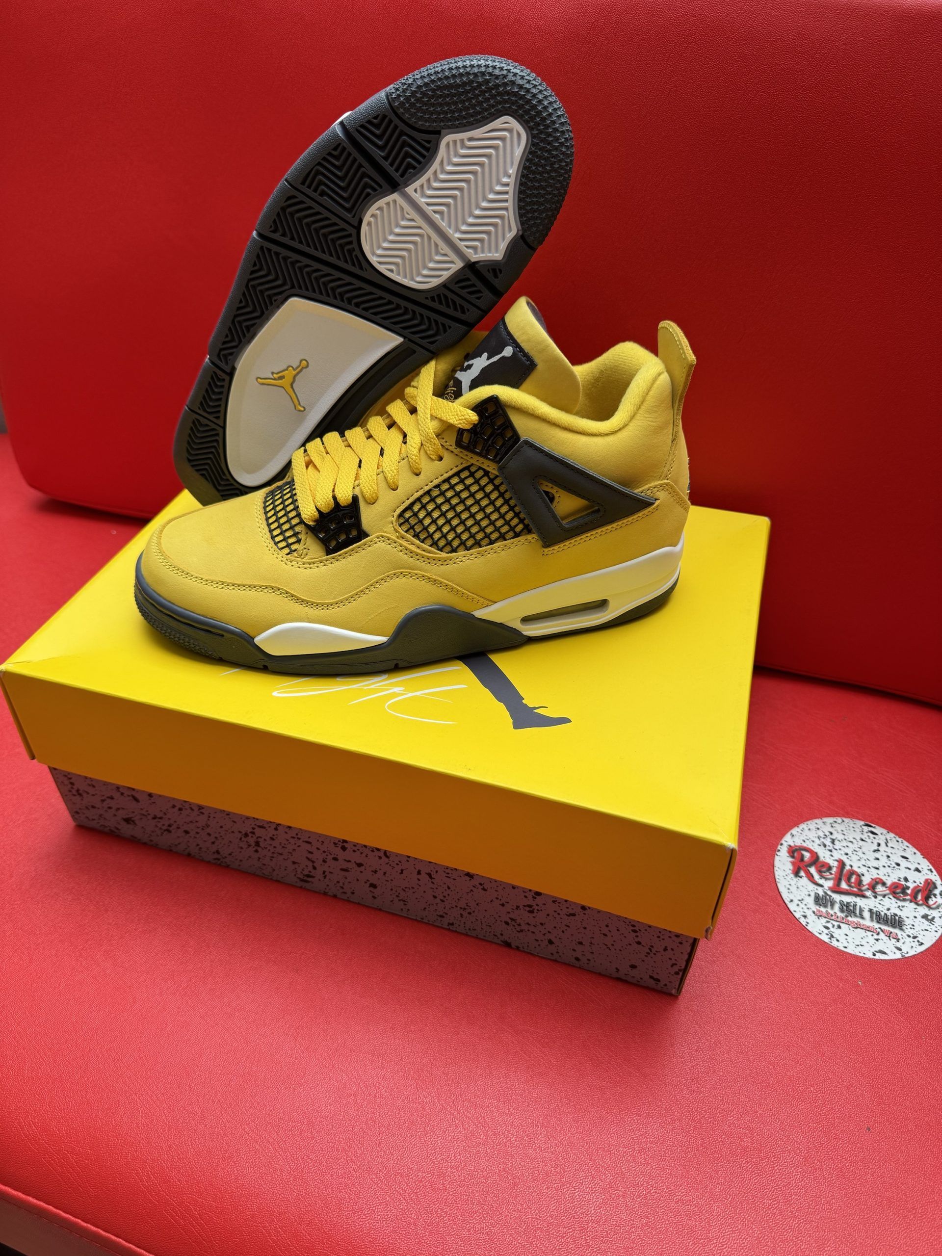 Yellow Air Jordan 4 sneaker with black accents, on its box, sole up.