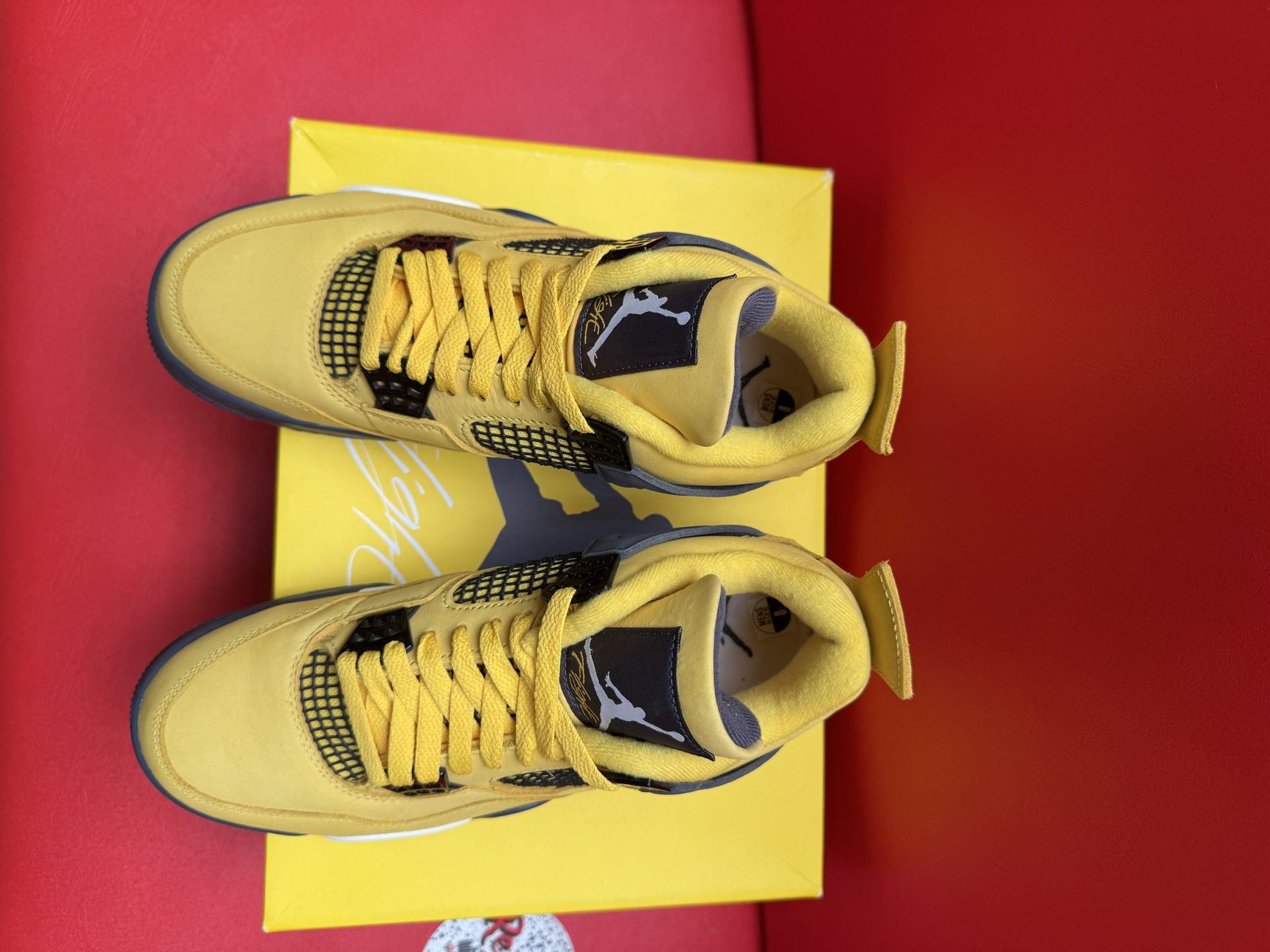 Yellow Air Jordan 4 sneaker with black accents, on its box, sole up.