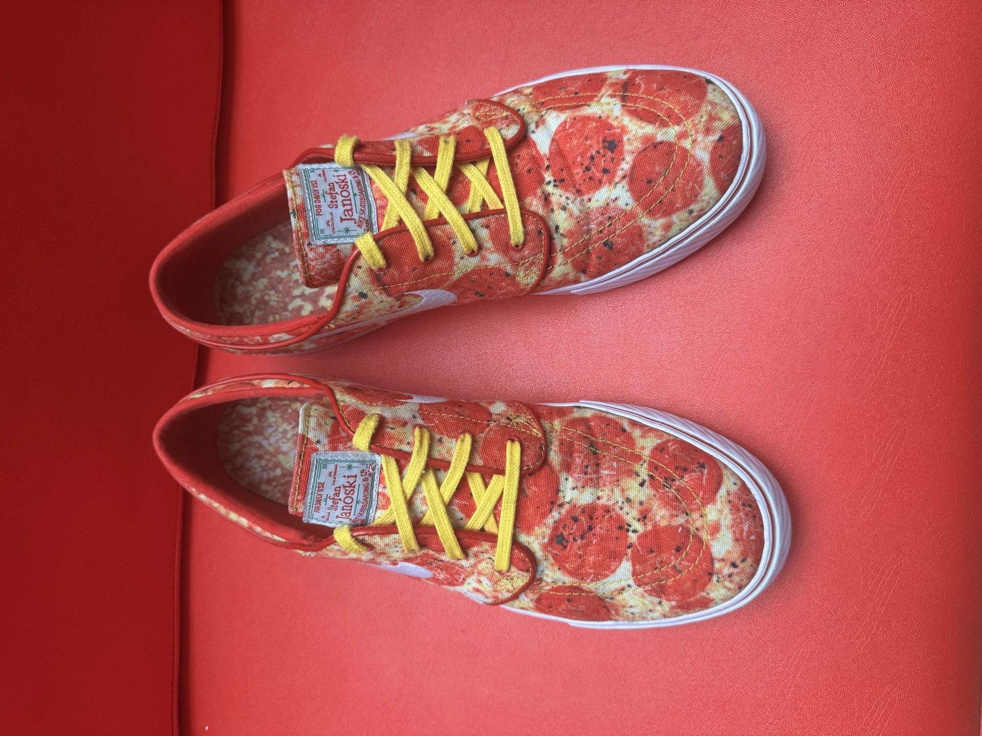 Pizza-themed Nike skate shoes with a red, white, and yellow color scheme, sitting on a red surface.