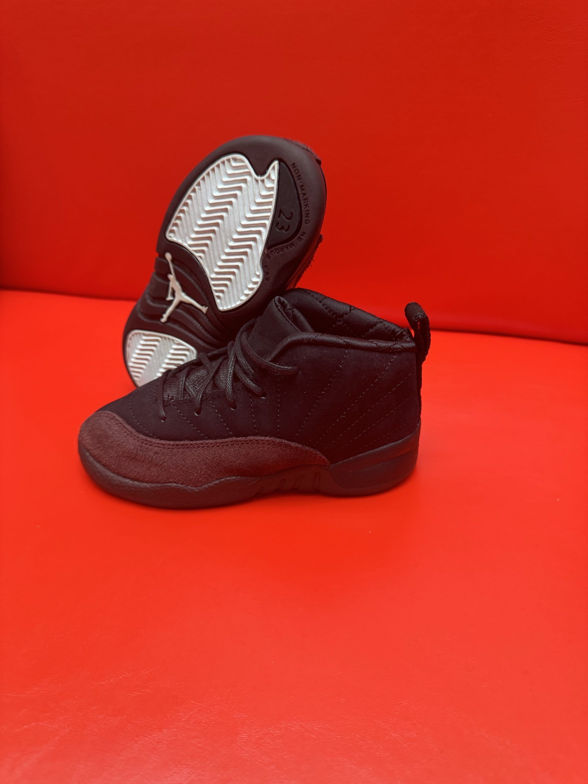 Black toddler-sized Air Jordan 12 sneakers on a red background.