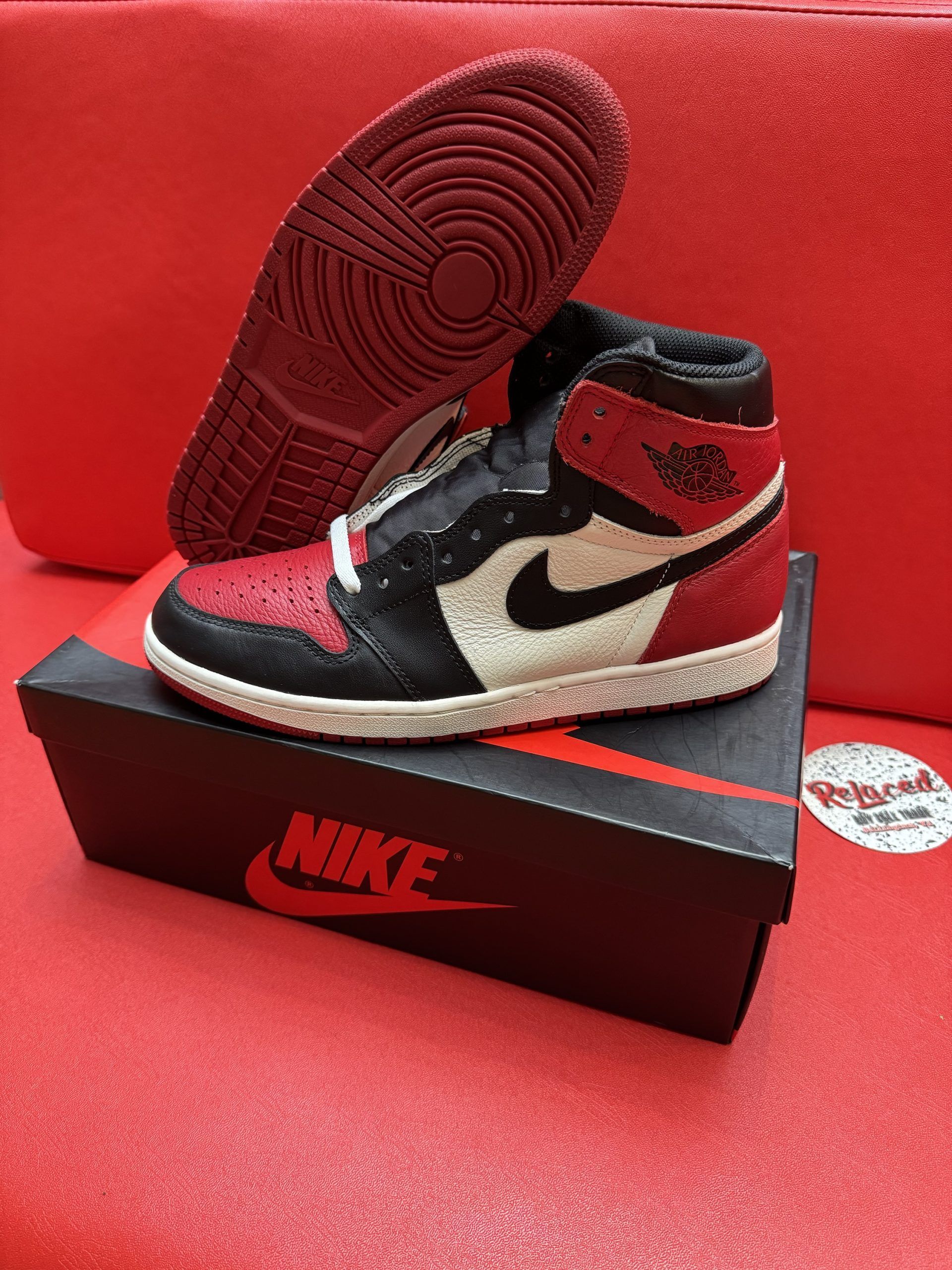 Black, red, and white Air Jordan 1 sneaker on box, sole visible, against a red surface.