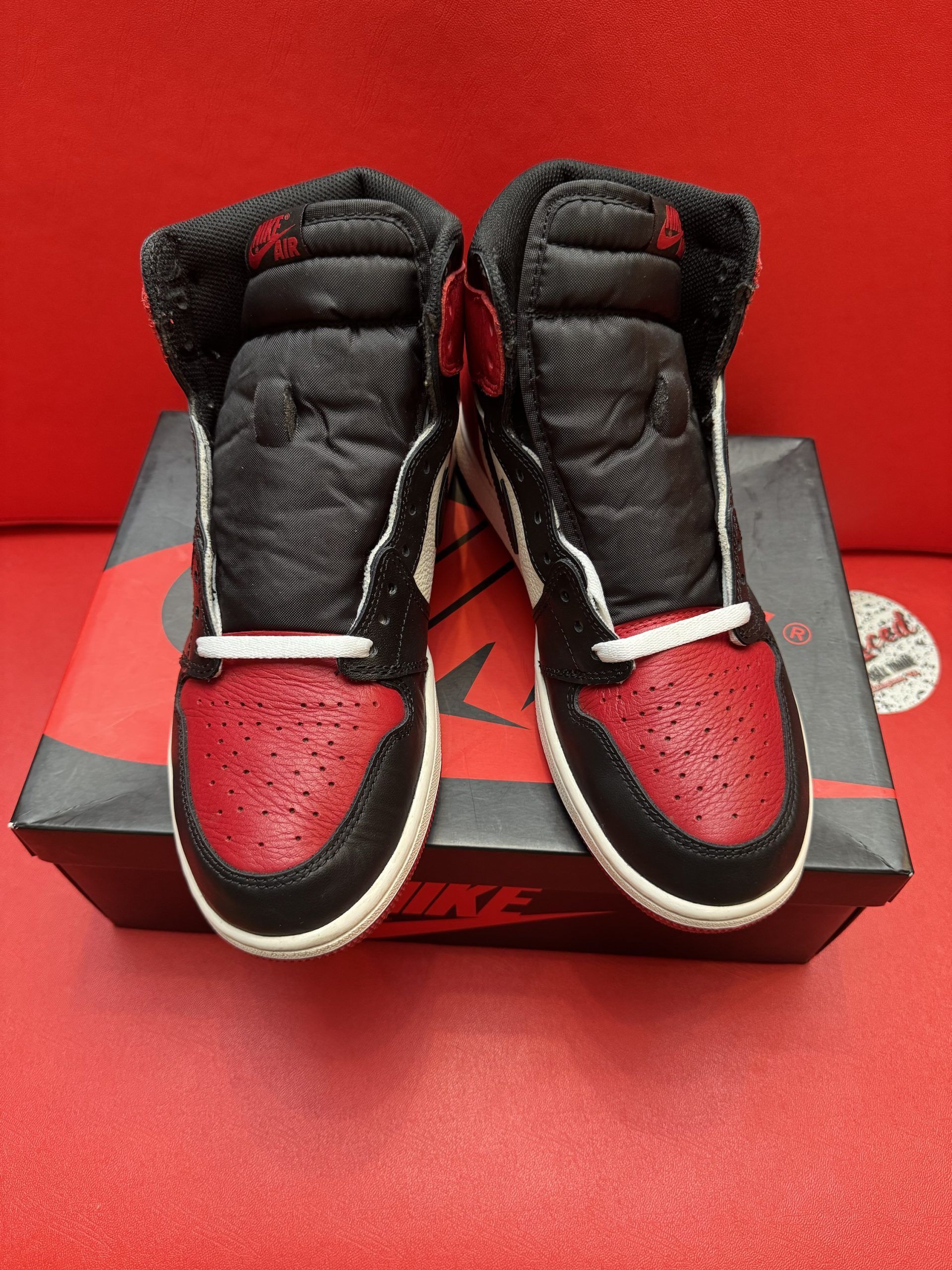 Black, red, and white Air Jordan 1 sneaker on box, sole visible, against a red surface.