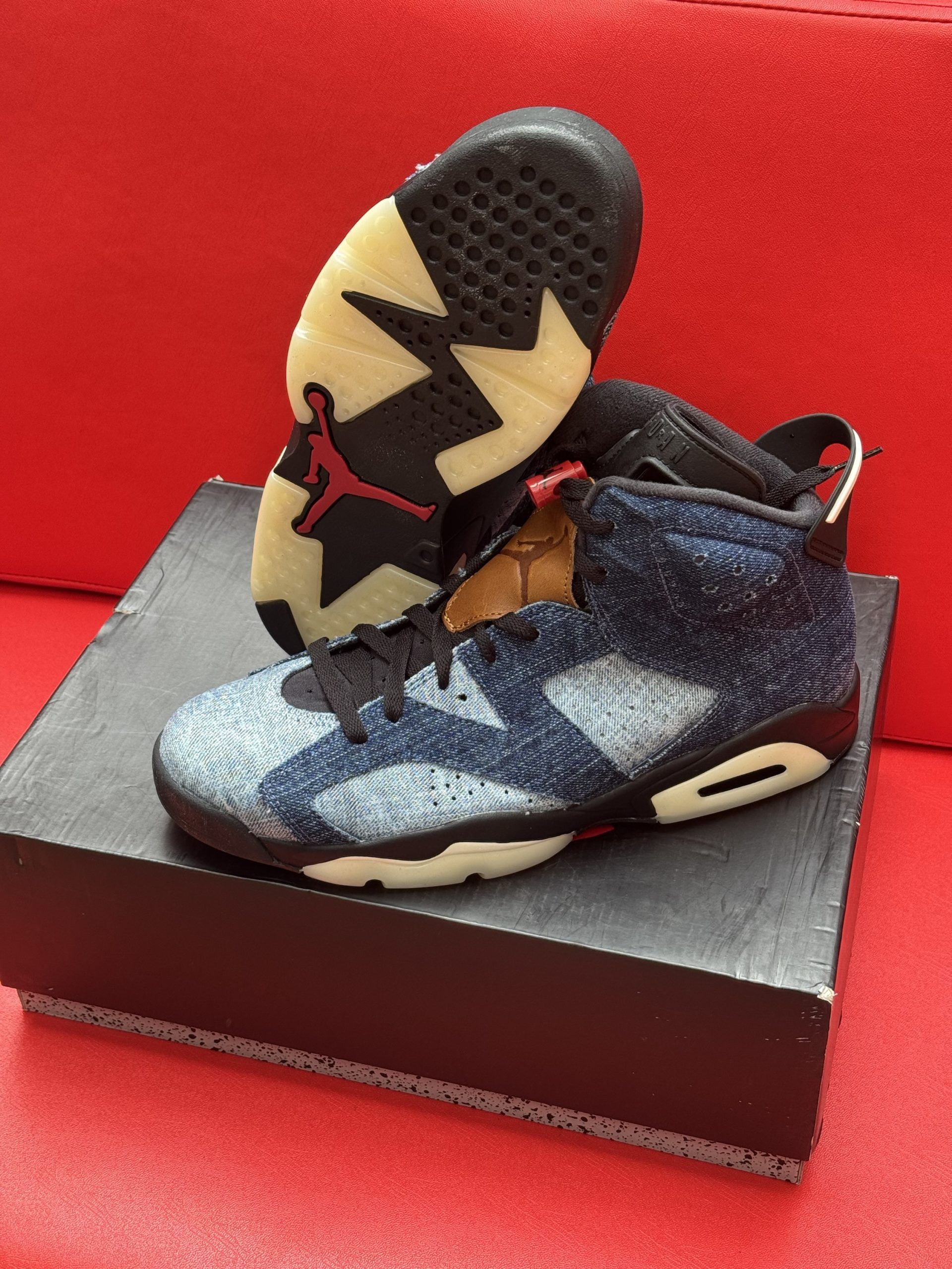 Pair of blue denim Jordan 6 sneakers on top of a black shoebox, with one shoe's sole visible.
