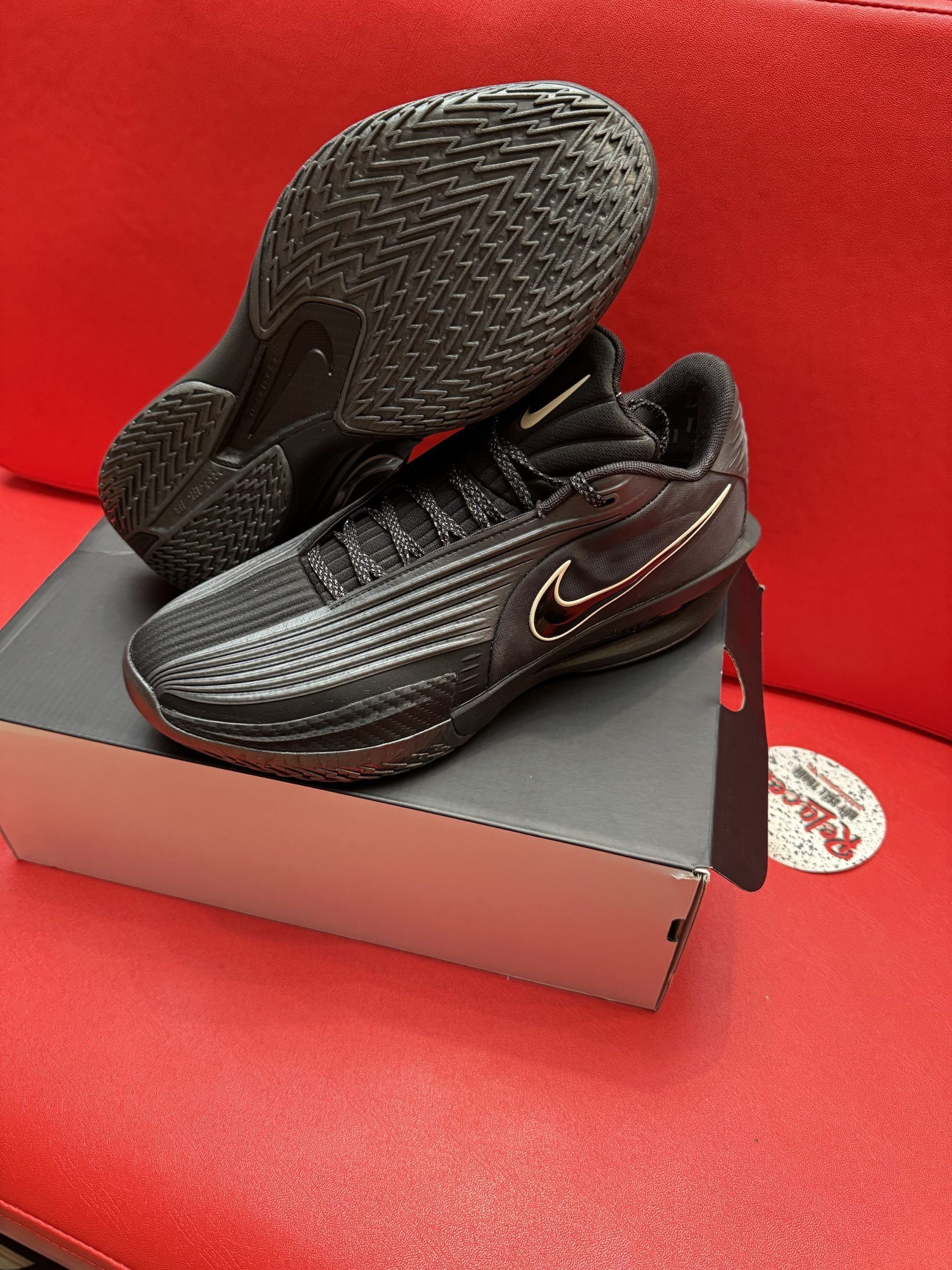 Black Nike athletic shoes on a box, sole up, set on a red surface.
