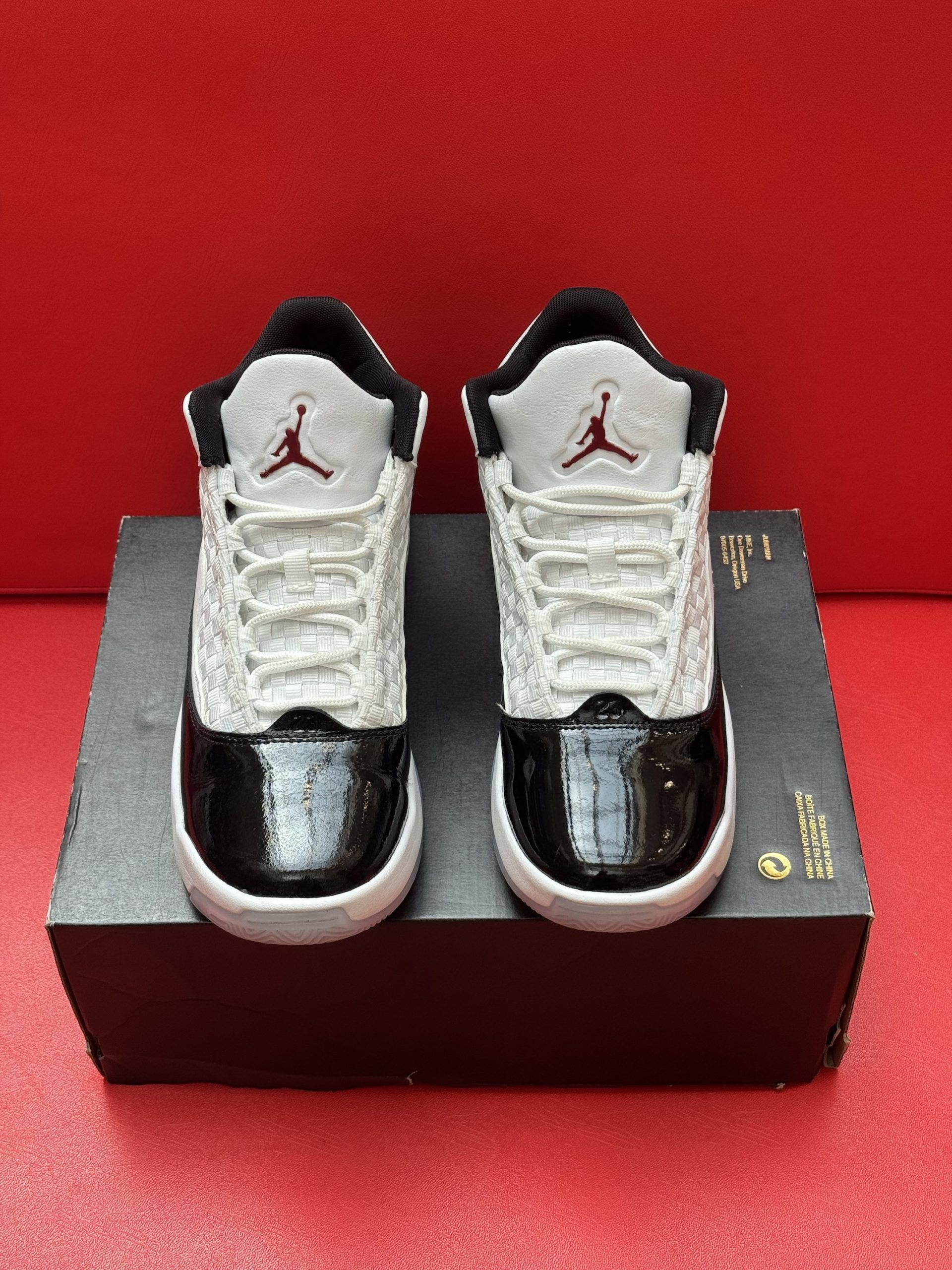 Black and white Air Jordan sneakers on a shoebox against a red background.