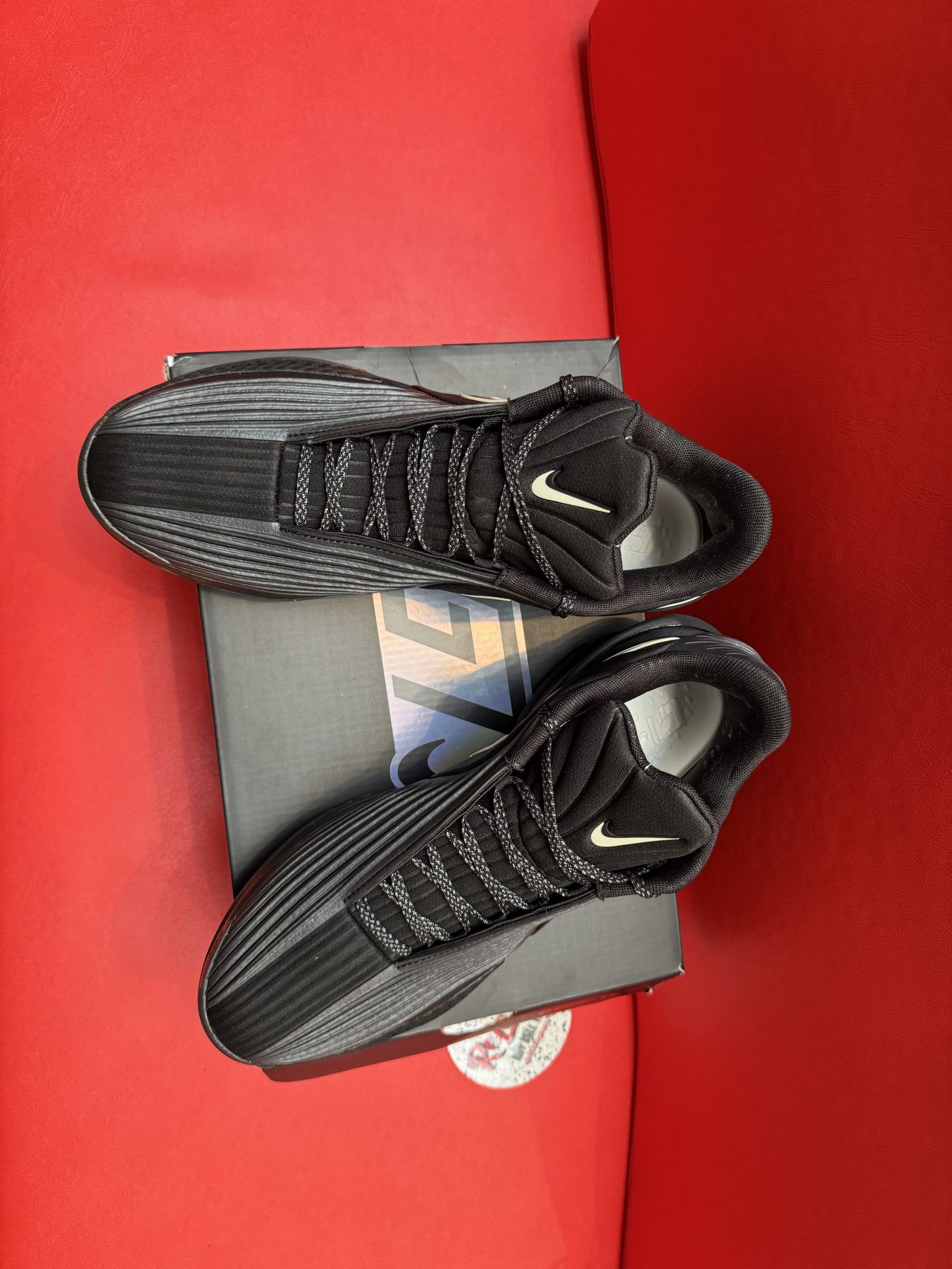 Black Nike athletic shoes on a box, sole up, set on a red surface.