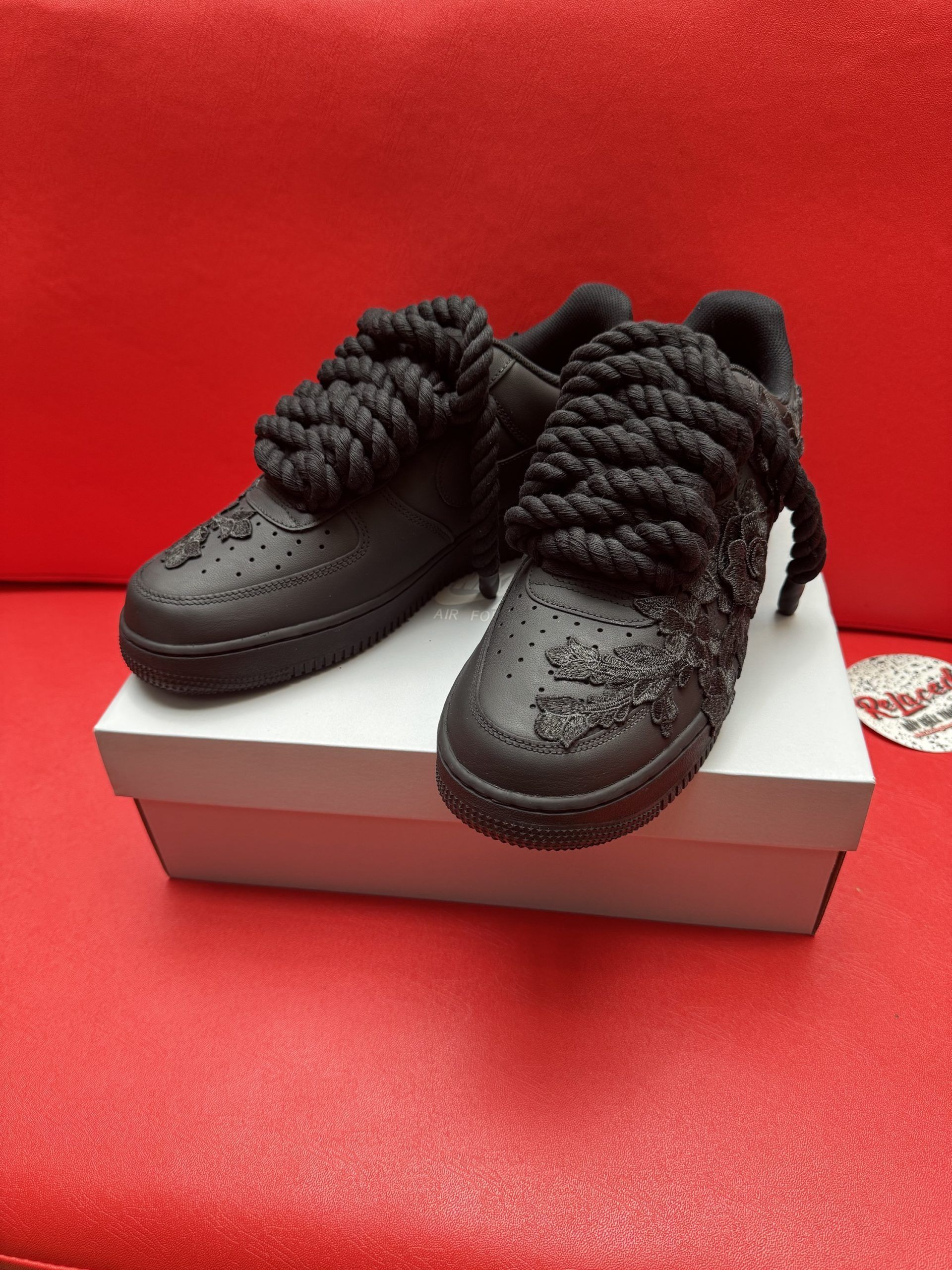 Black textured sneakers on white box, red background. Sole of one shoe visible.