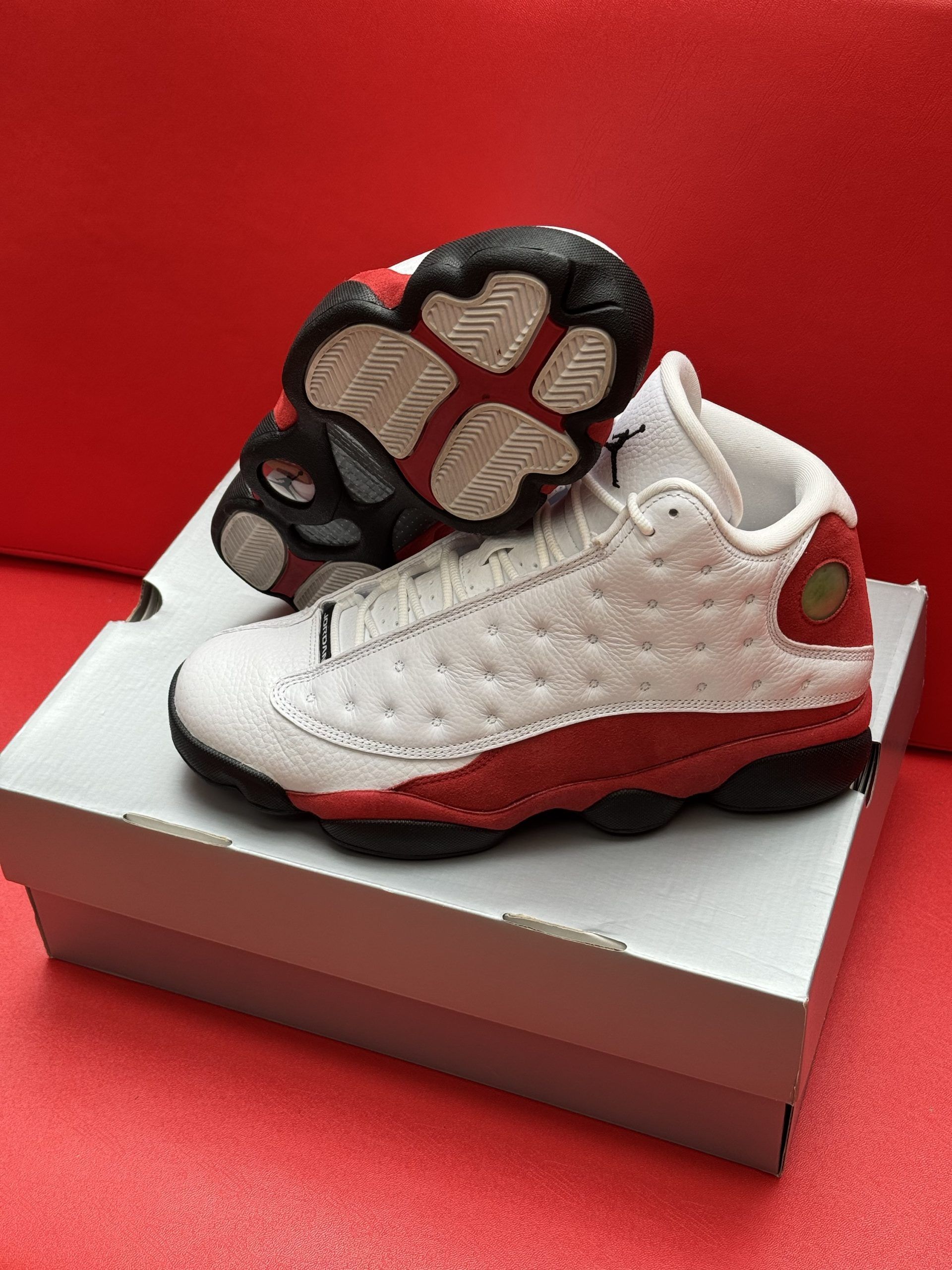 White and red Air Jordan 13 toddler sneakers on a box, red background.