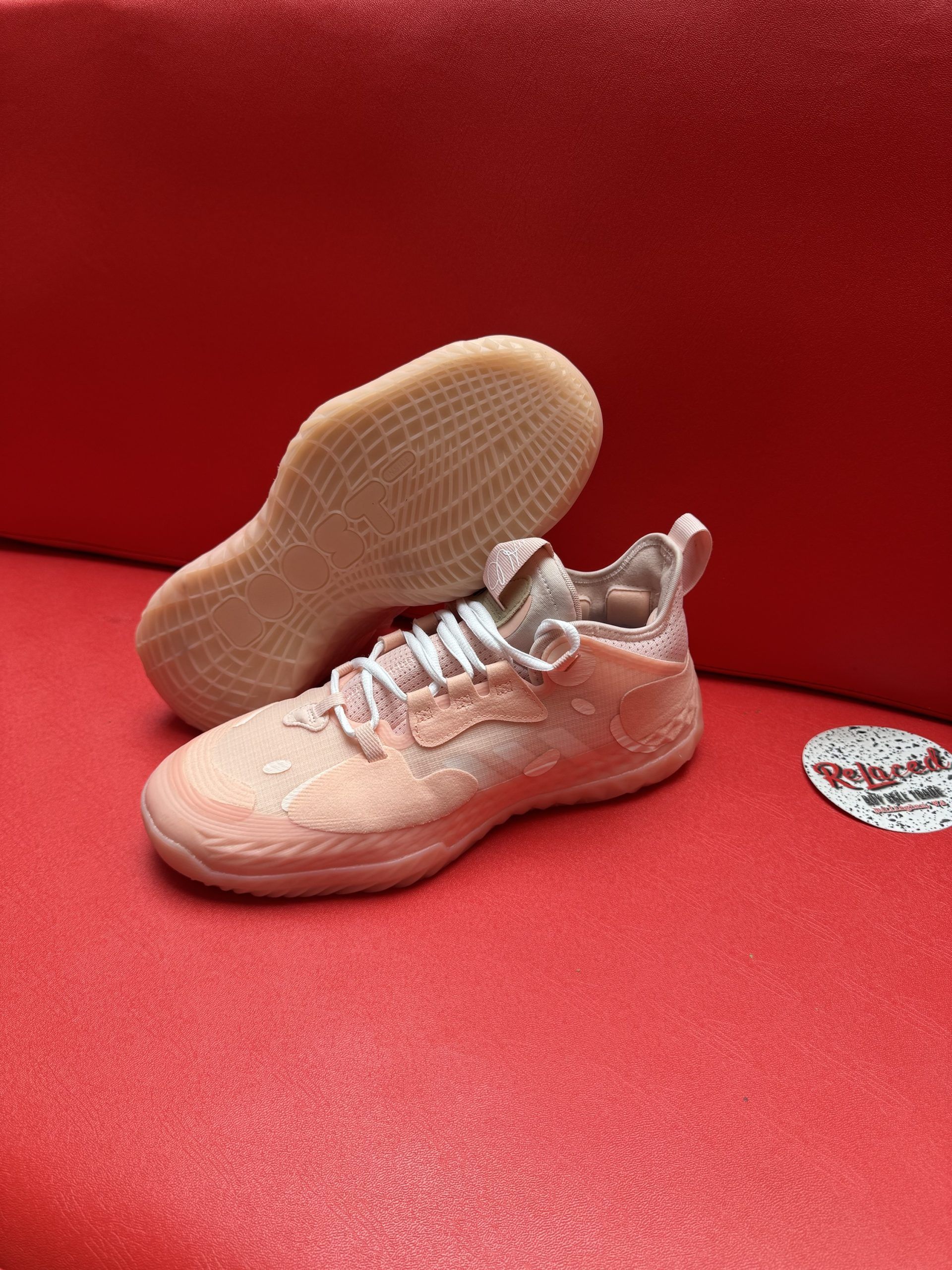 Pink athletic shoe with a textured sole, resting on a red surface.