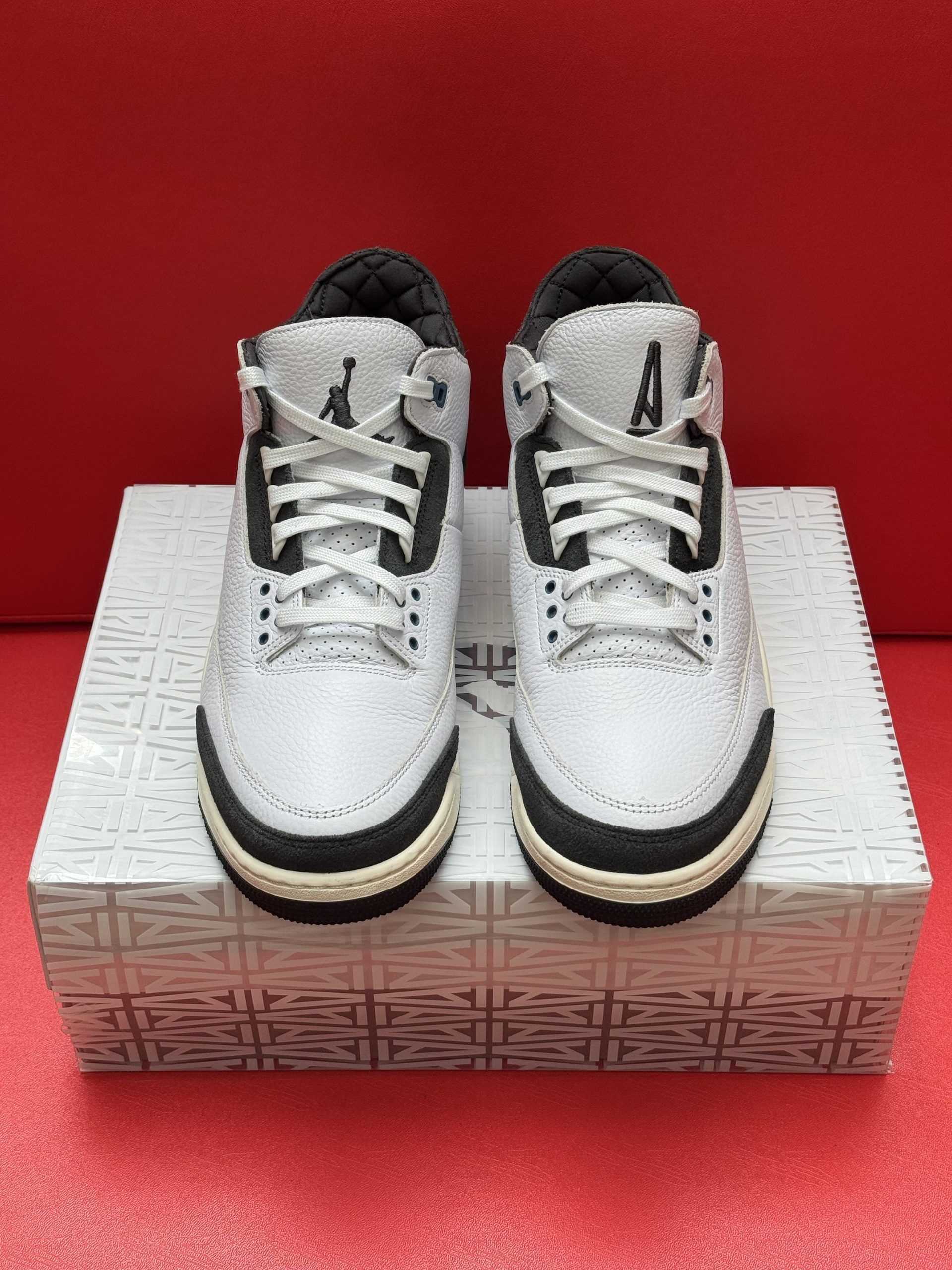 White and black Air Jordan 3 sneakers on a patterned box, against a red background.