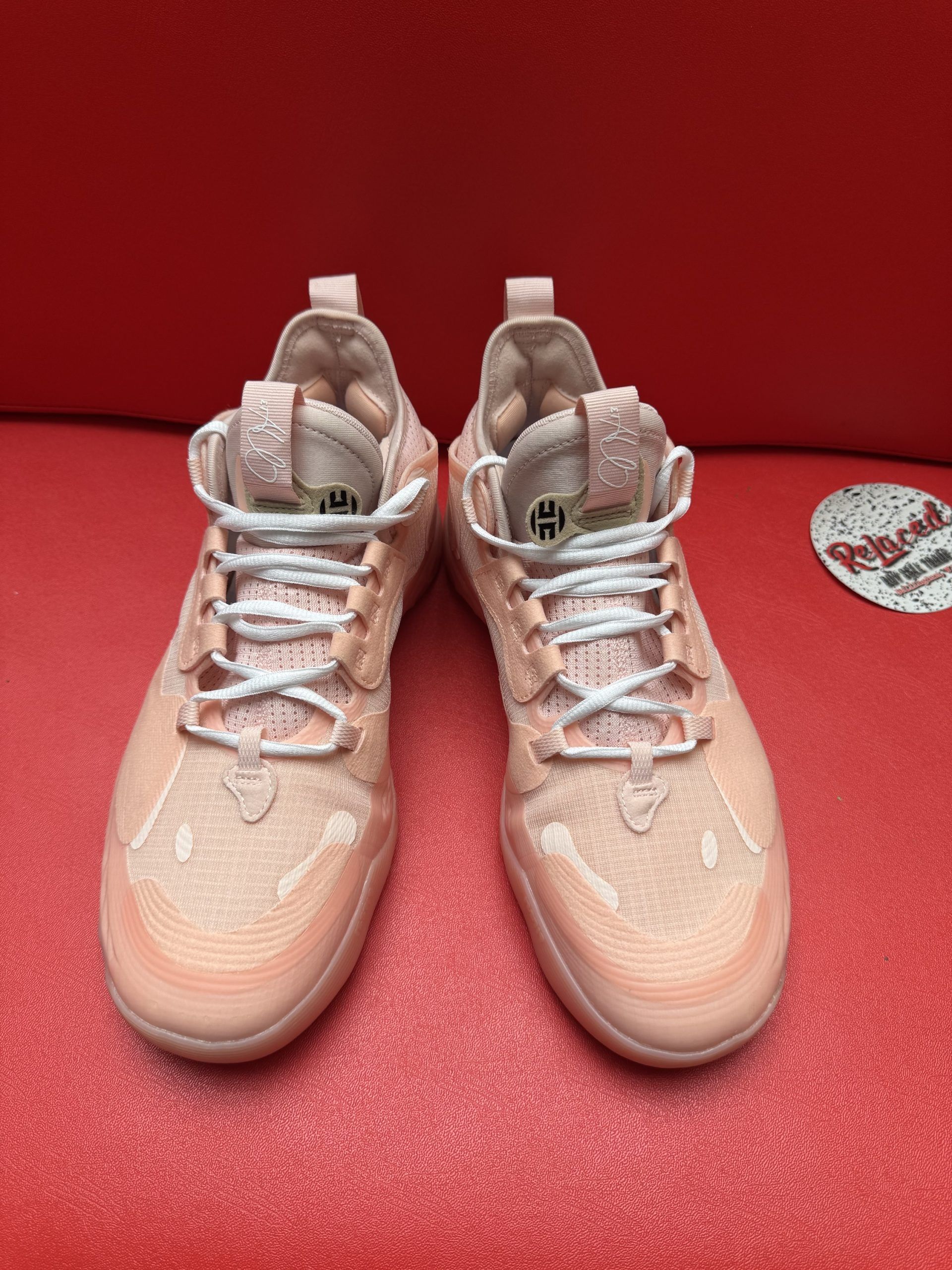 Pink athletic shoe with a textured sole, resting on a red surface.