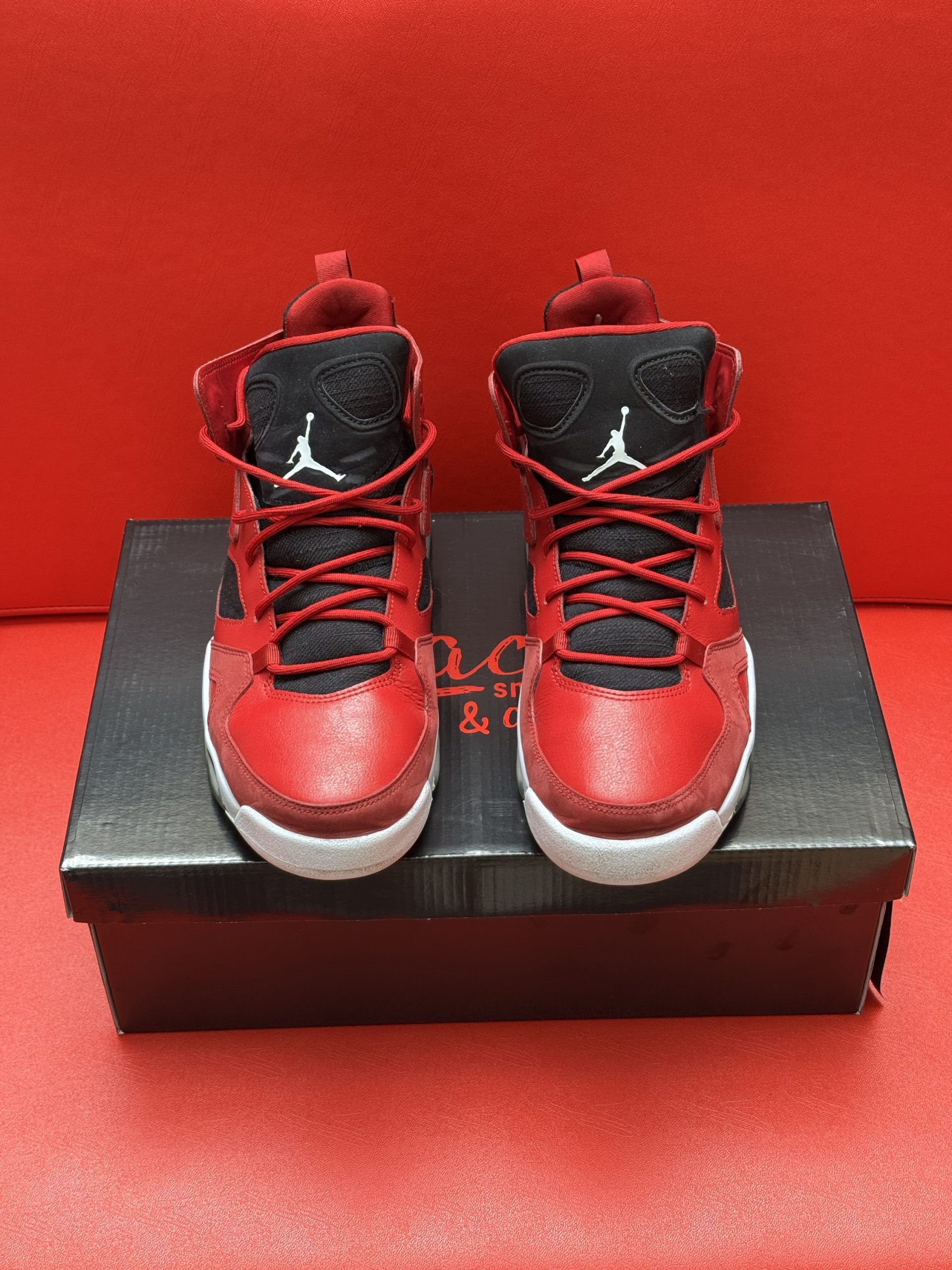 Red and black Air Jordan sneakers on a box against a red background. One sneaker is upside down.