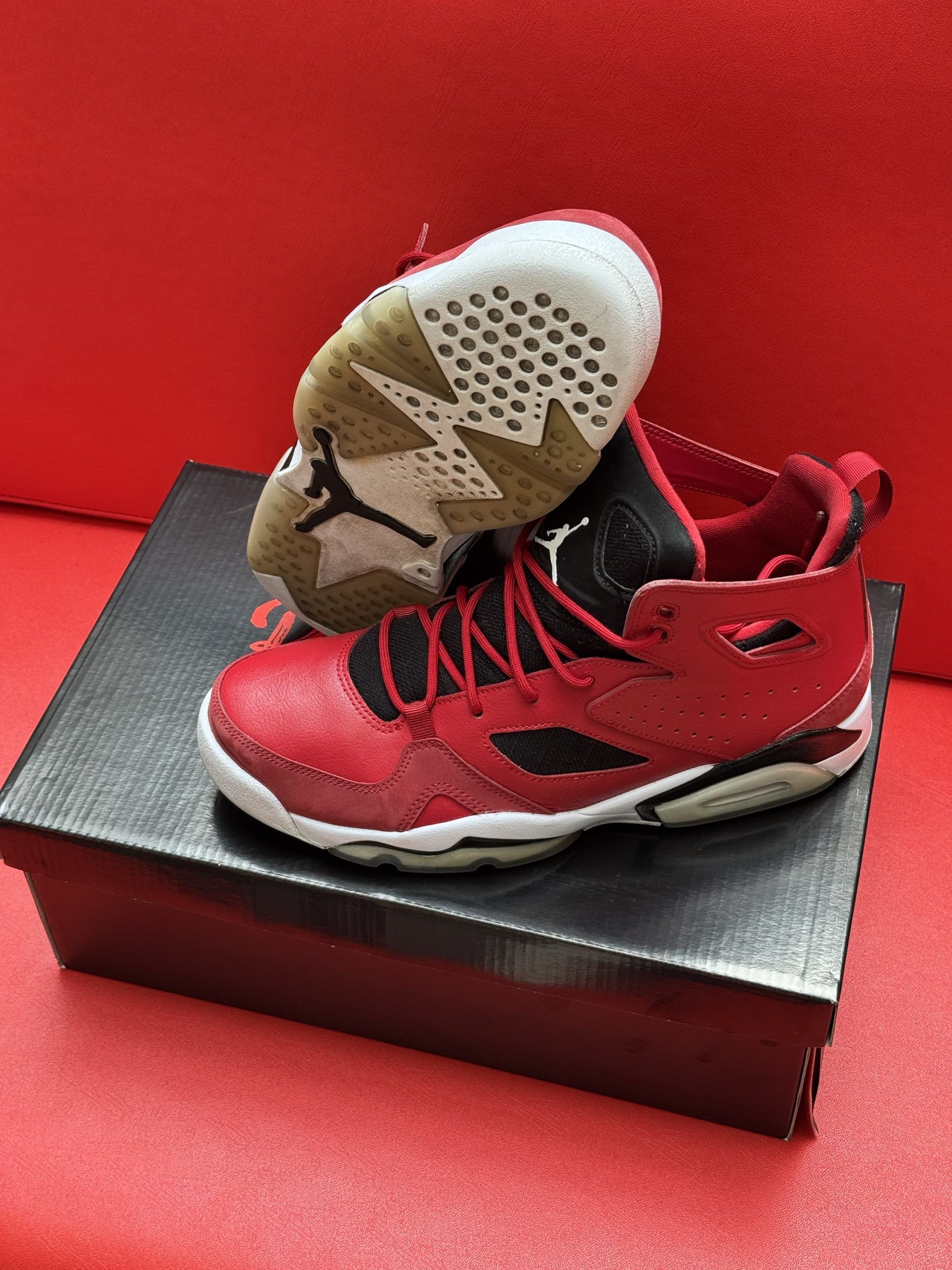 Red and black Air Jordan sneakers on a box against a red background. One sneaker is upside down.