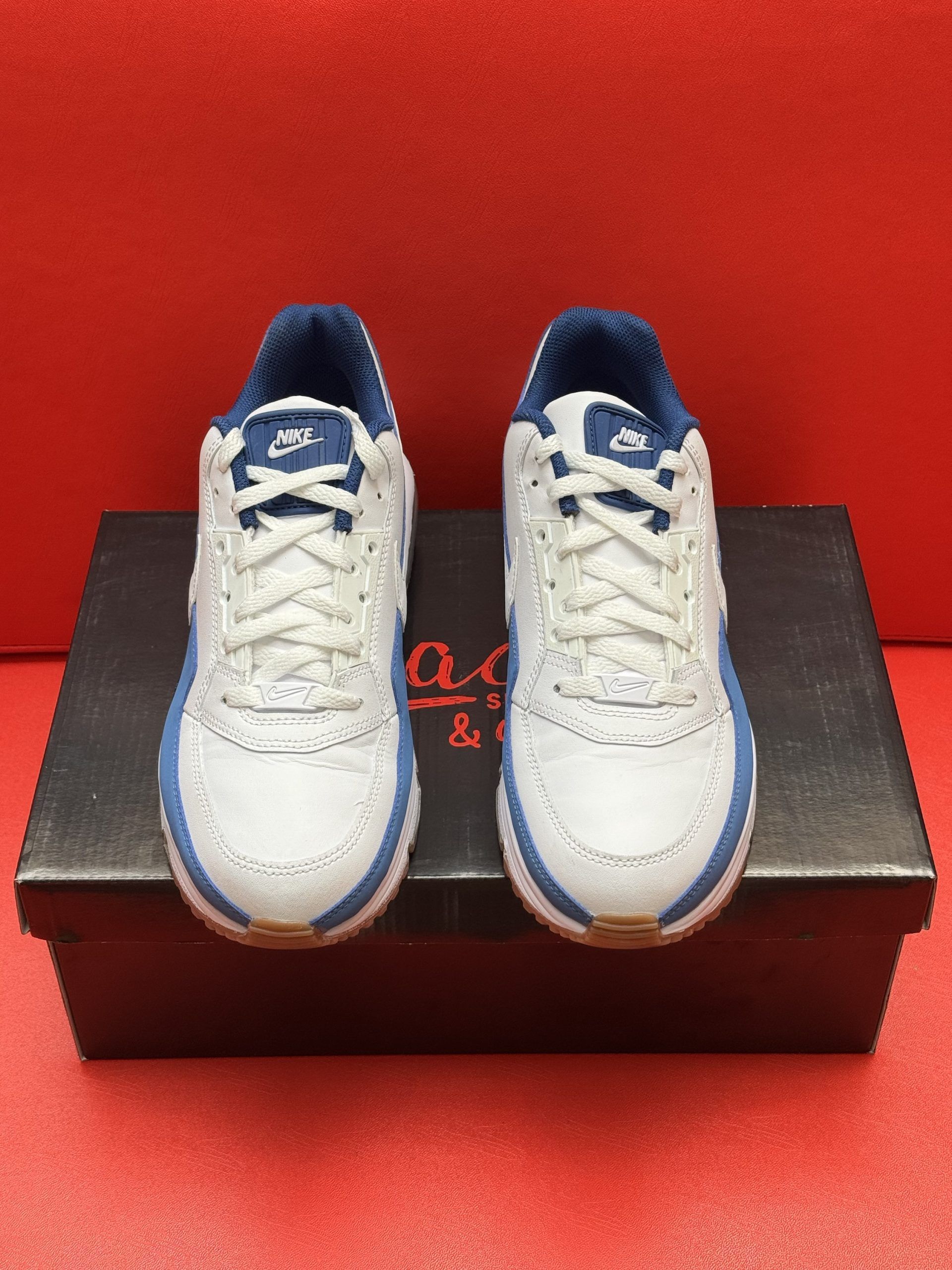 White and blue Nike Air Max sneakers on black box, against a red background.
