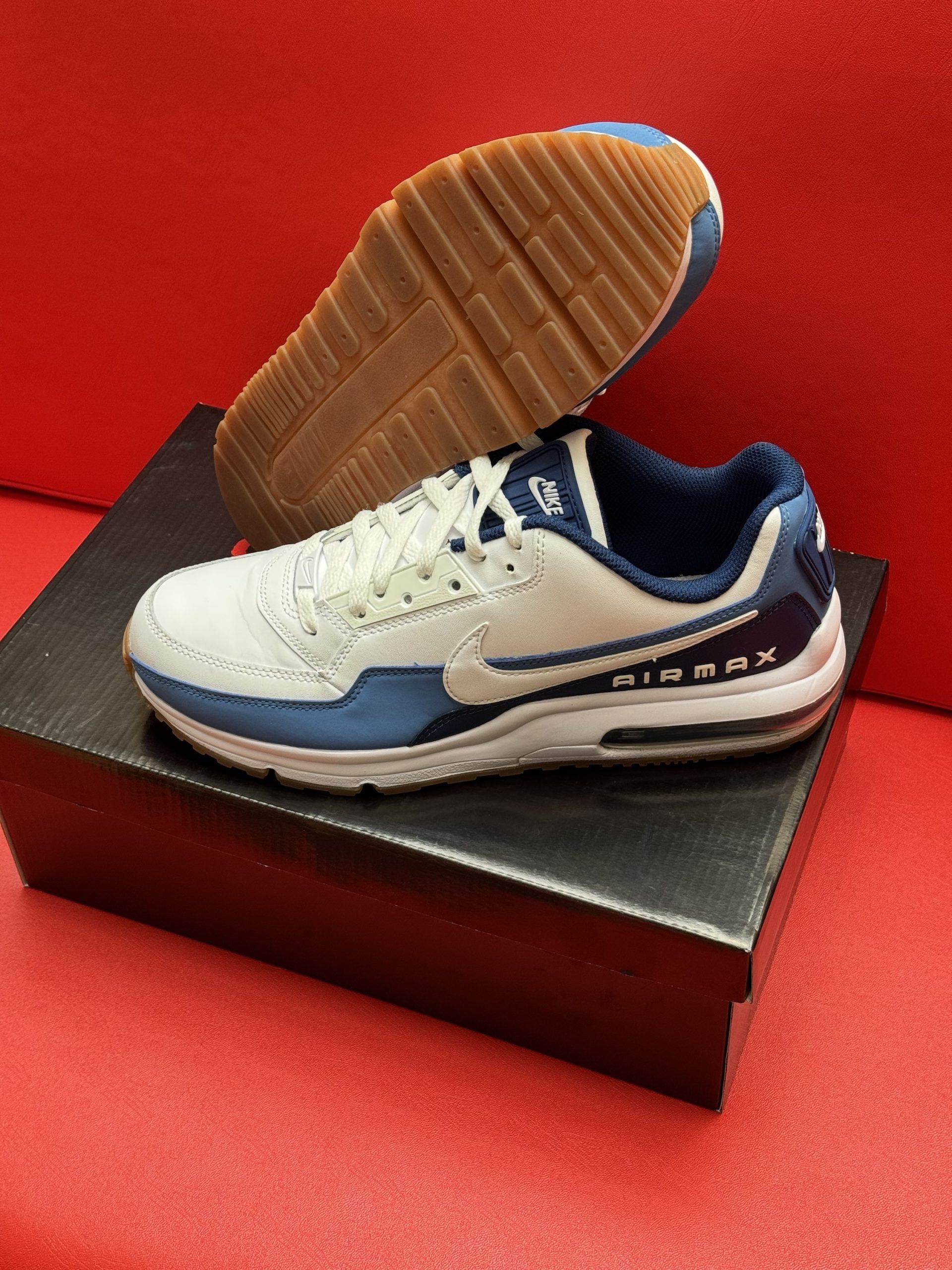 White and blue Nike Air Max sneakers on black box, against a red background.