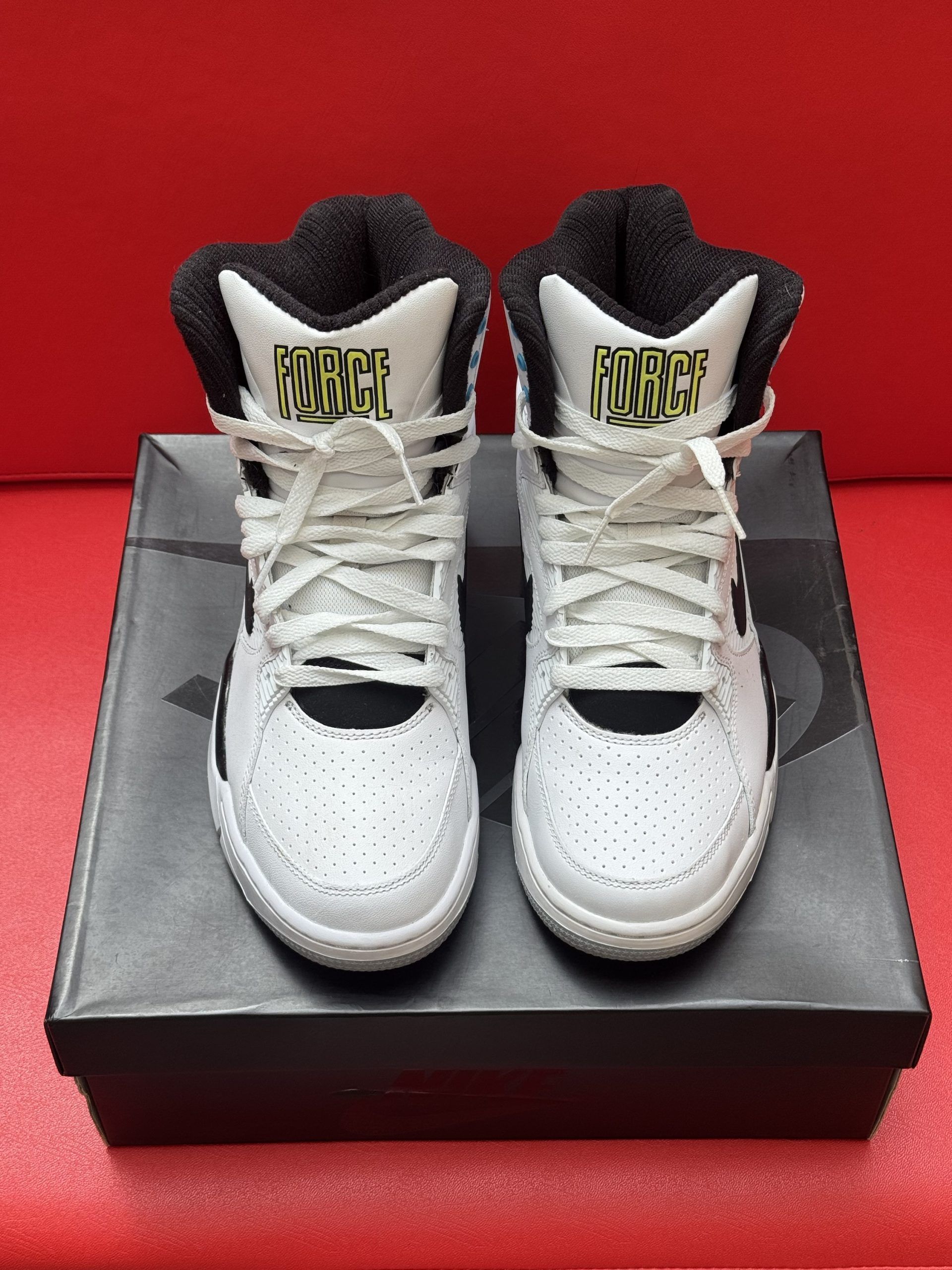 White Nike Air Force 180 sneakers, black box, red background.