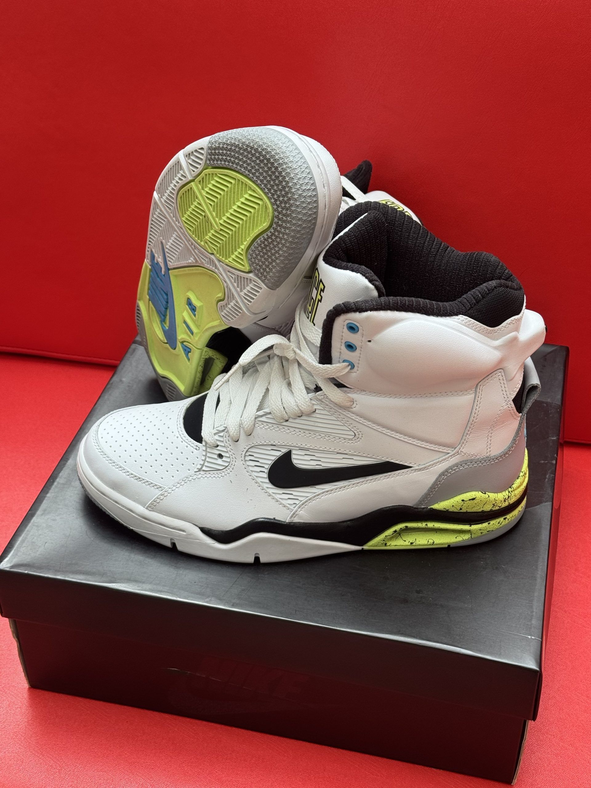 White Nike Air Force 180 sneakers, black box, red background.