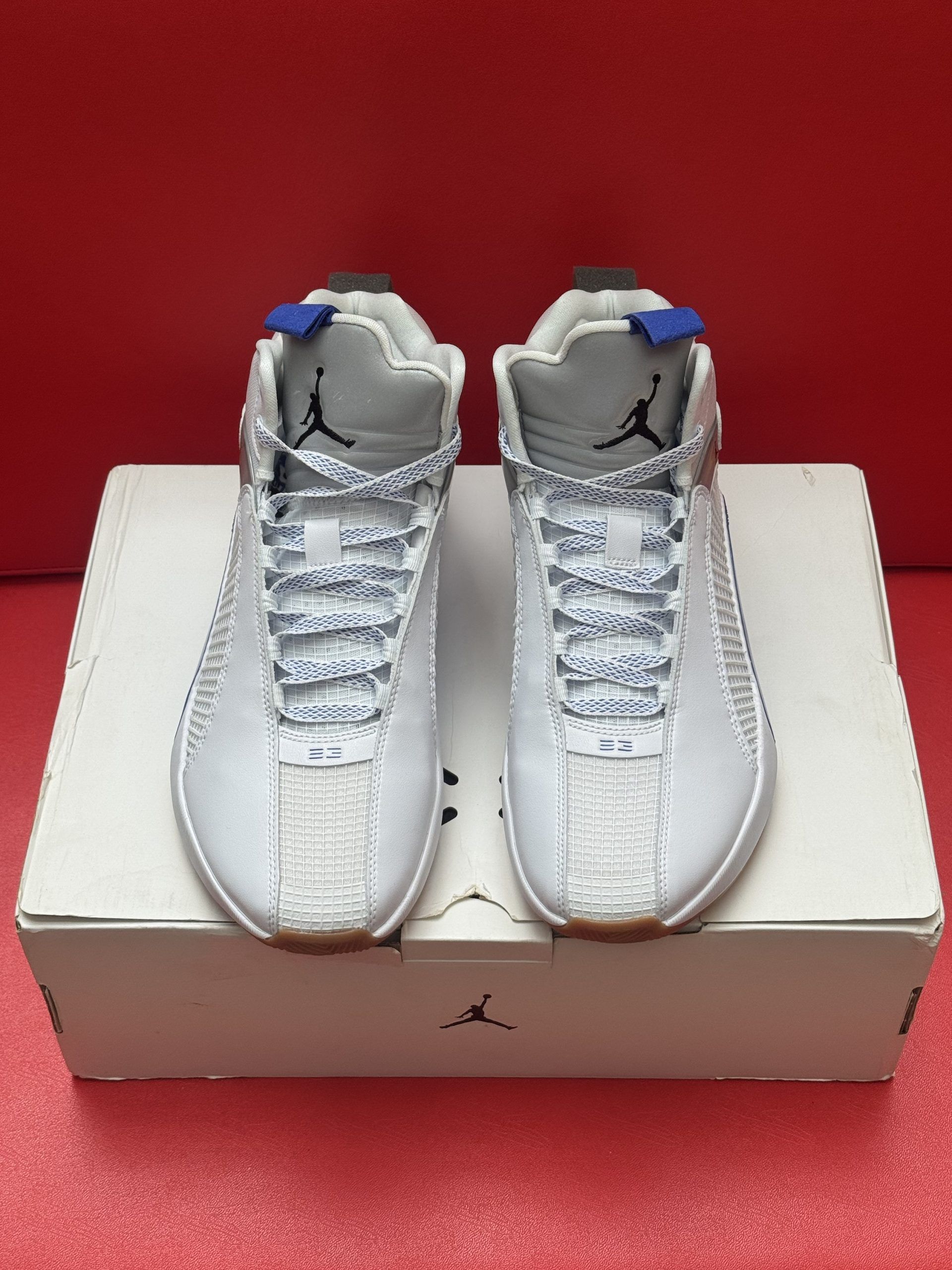 White and blue Air Jordan 35 sneakers on top of a shoebox, against a red background.