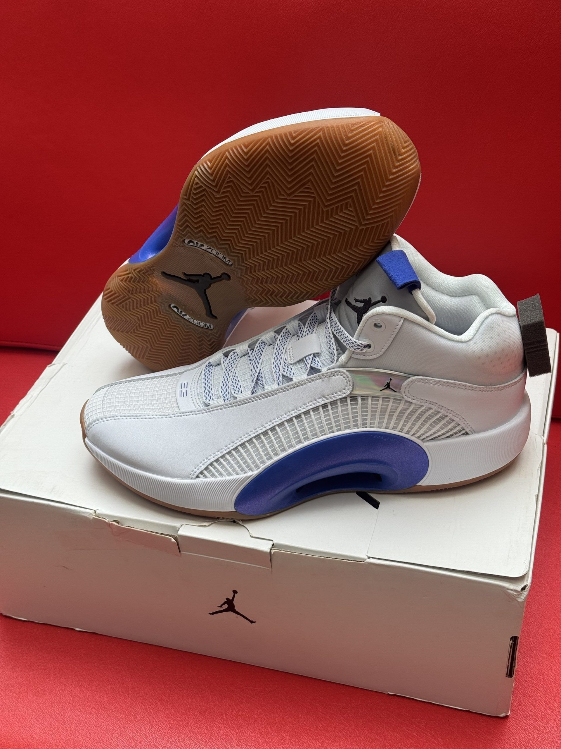White and blue Air Jordan 35 sneakers on top of a shoebox, against a red background.