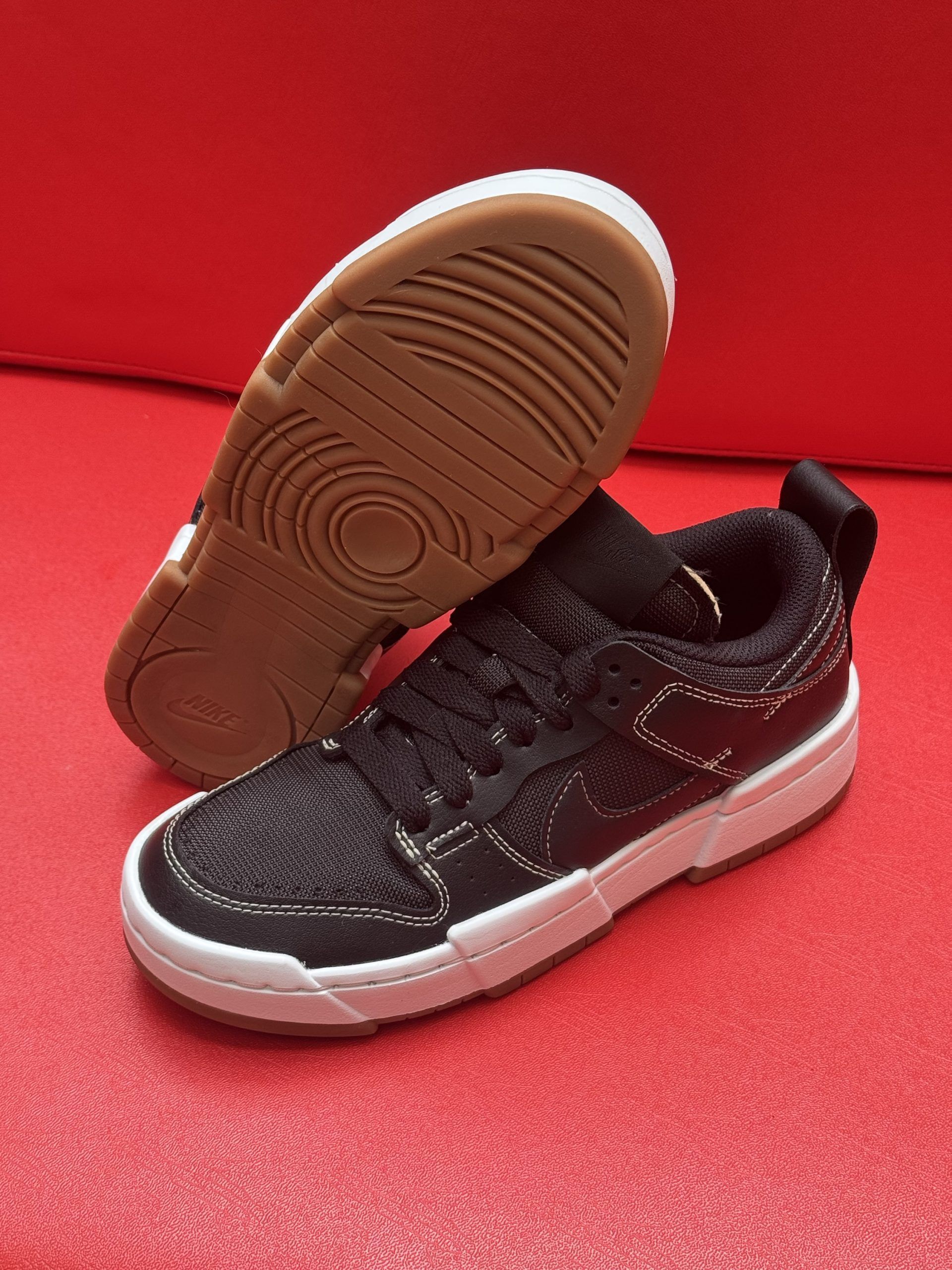Black and white sneakers with brown sole on red background.