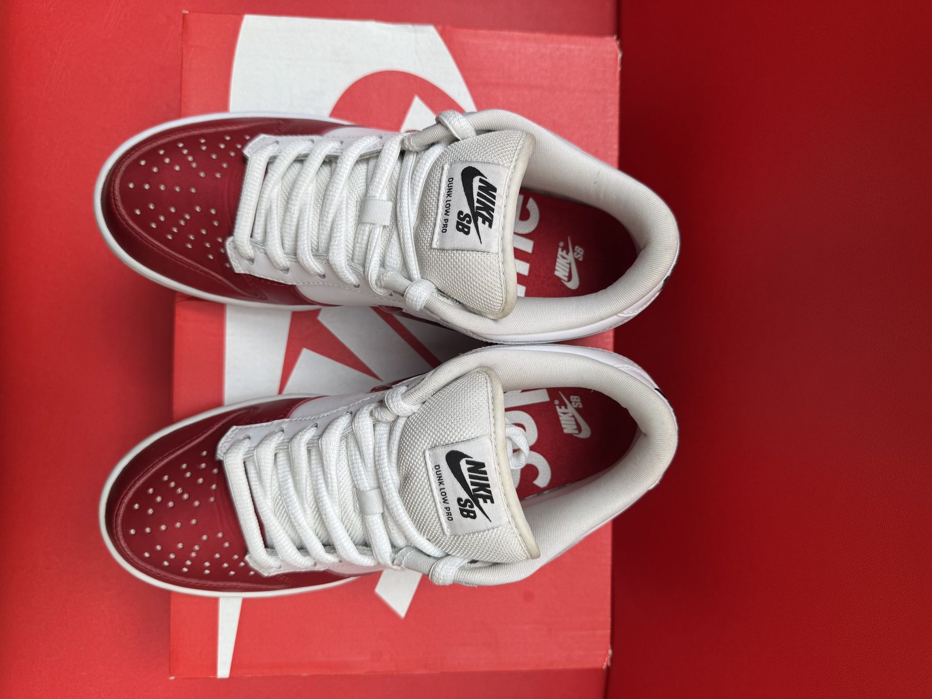Red and white Nike SB Dunk Low sneakers with a star detail, on a red Nike box, against a red backdrop.