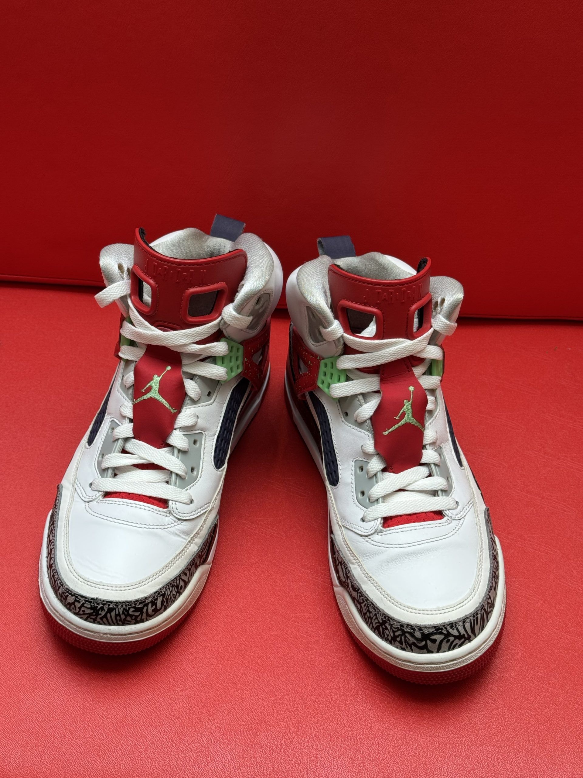 White, red, and blue Air Jordan sneakers on a red surface, showcasing the sole with green and red accents.