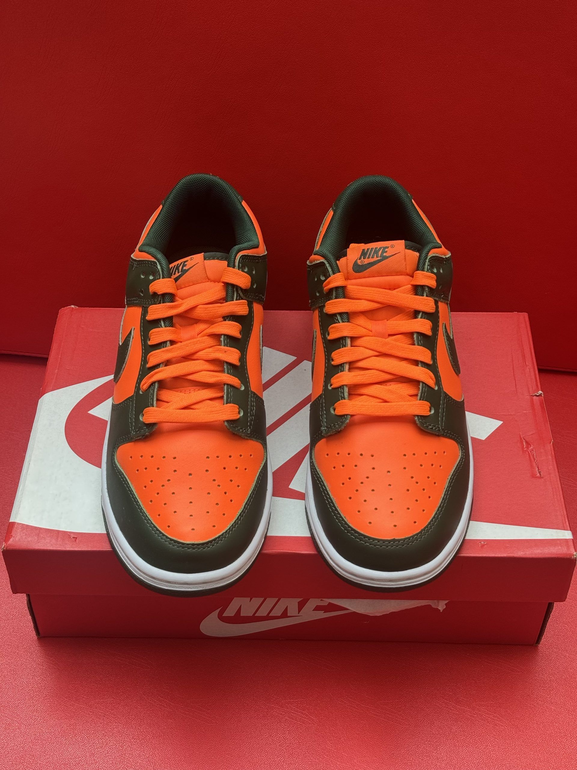 Orange and dark green Nike Dunk Low sneakers, box in the foreground, sole up.
