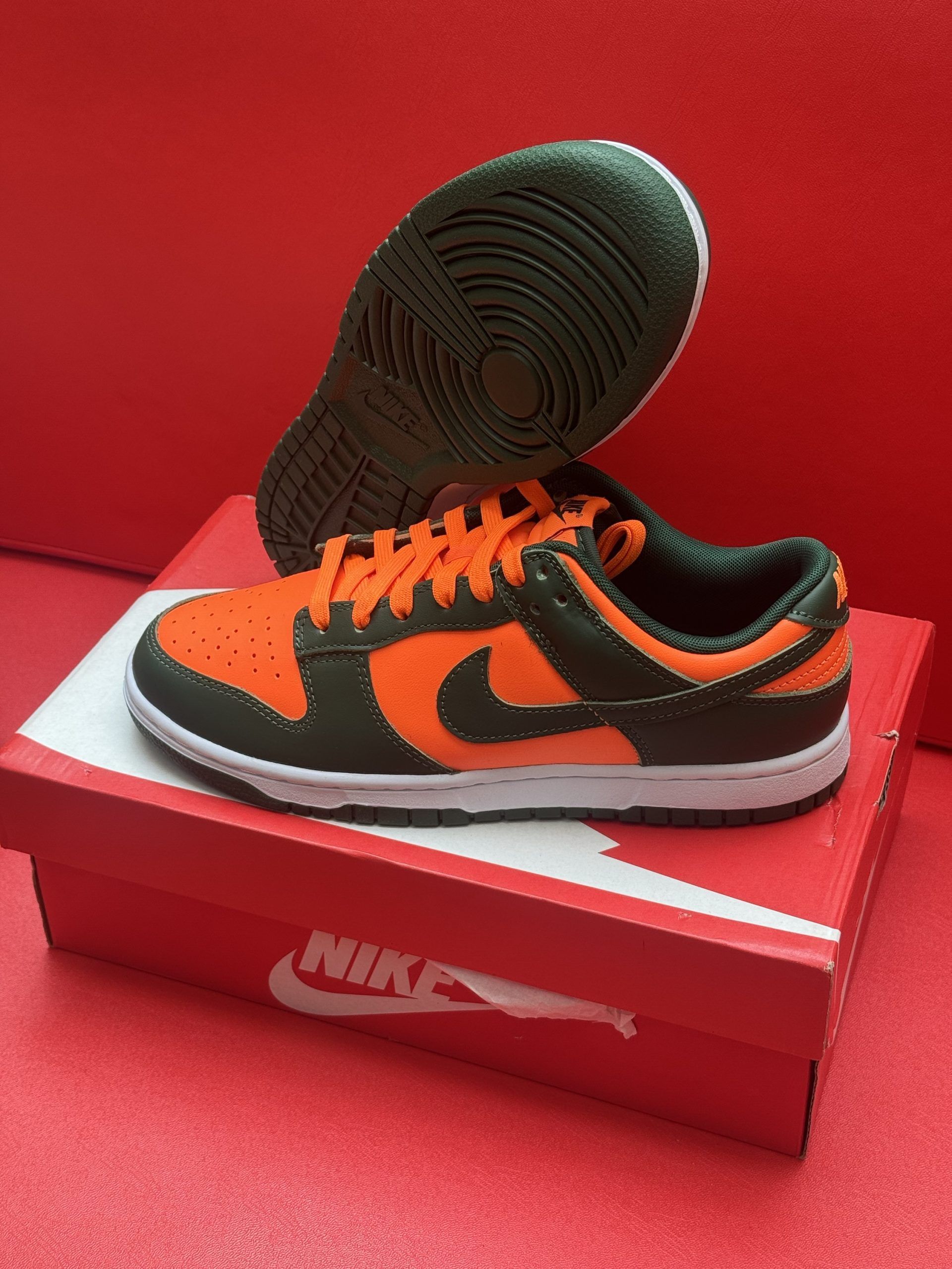 Orange and dark green Nike Dunk Low sneakers, box in the foreground, sole up.