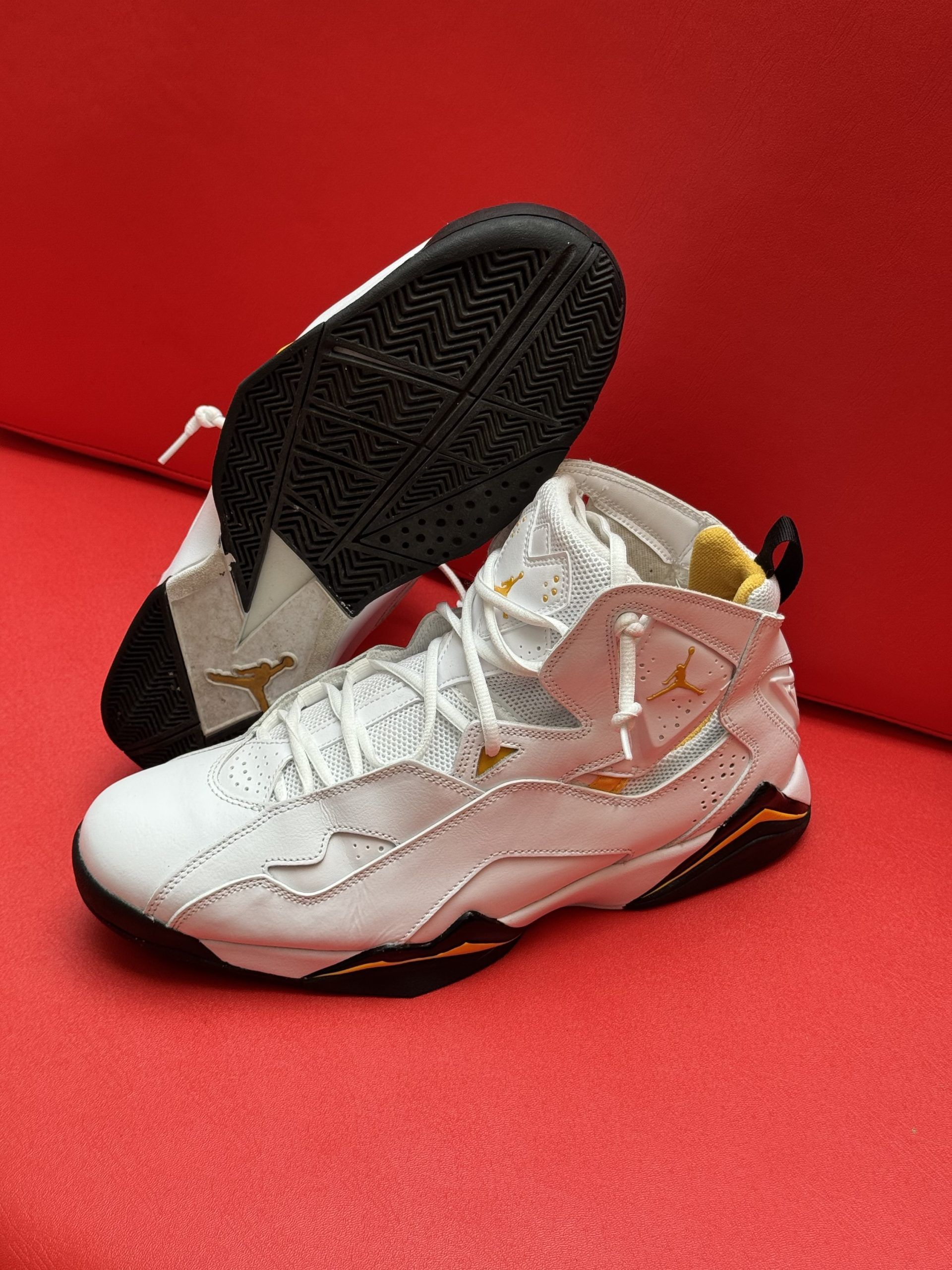 White and gold basketball shoes on a red surface; one shoe is upside down.