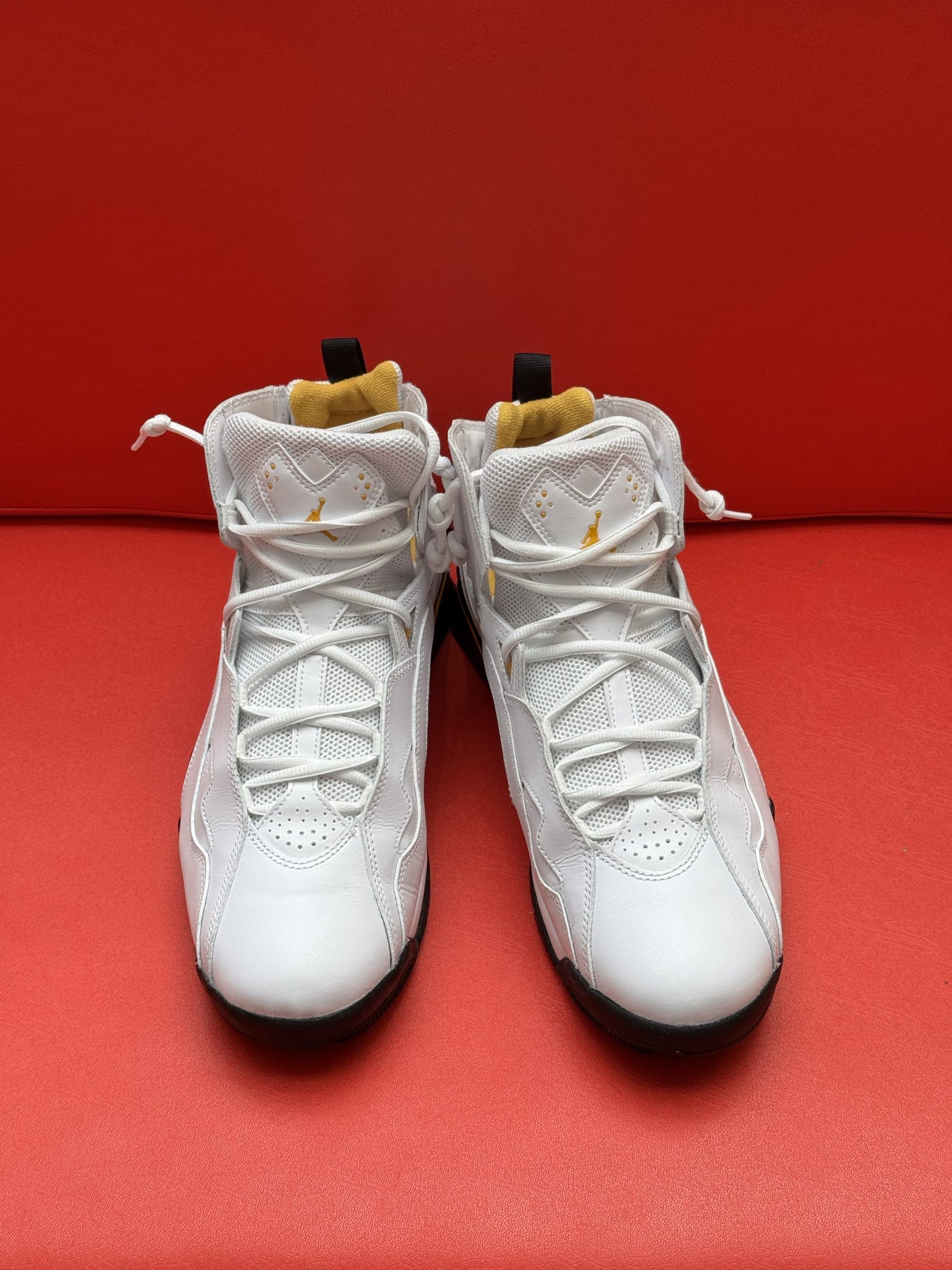 White and gold basketball shoes on a red surface; one shoe is upside down.