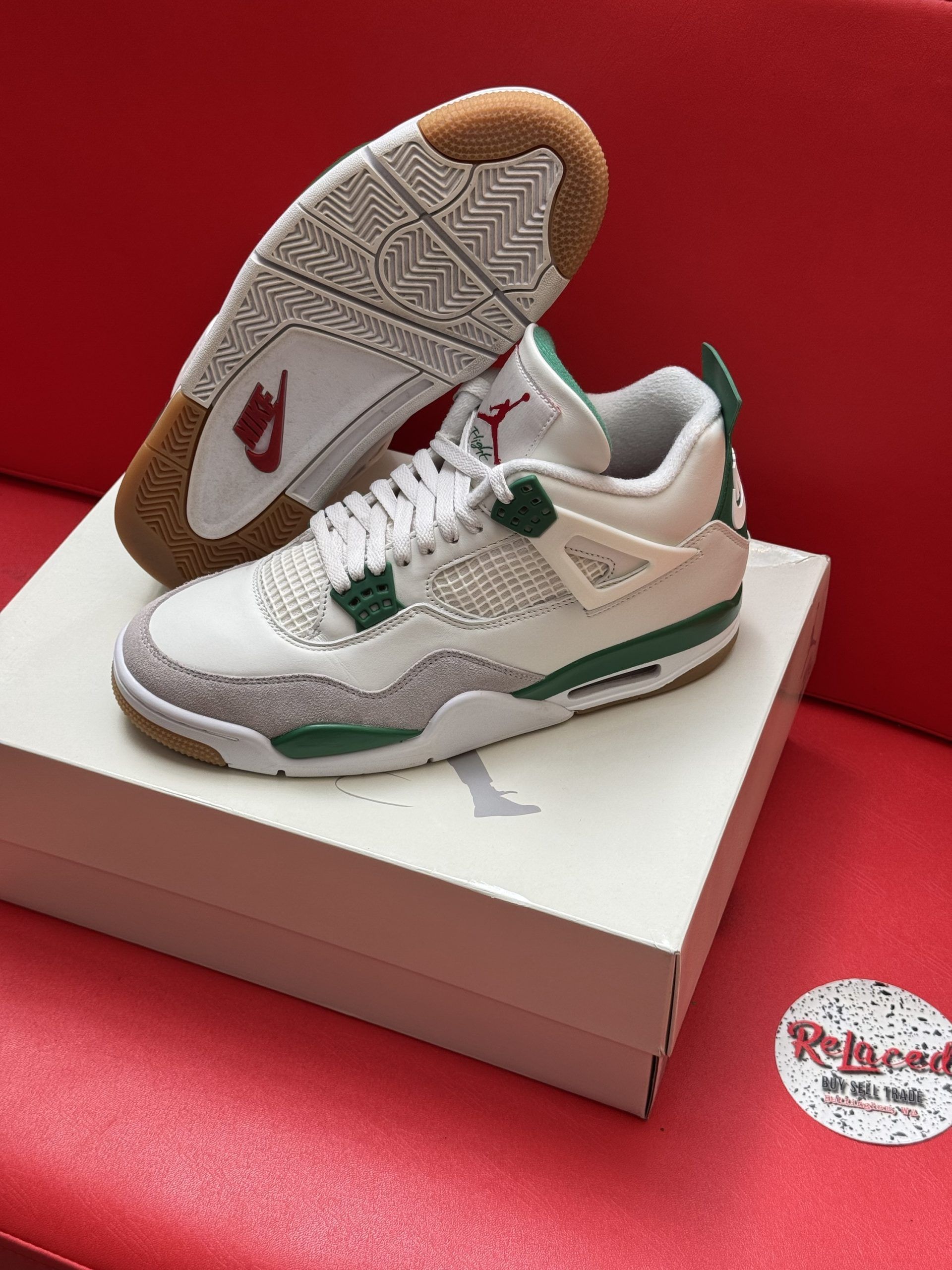 White, green, and grey Air Jordan 4 sneakers on a box, red background. Gum soles.