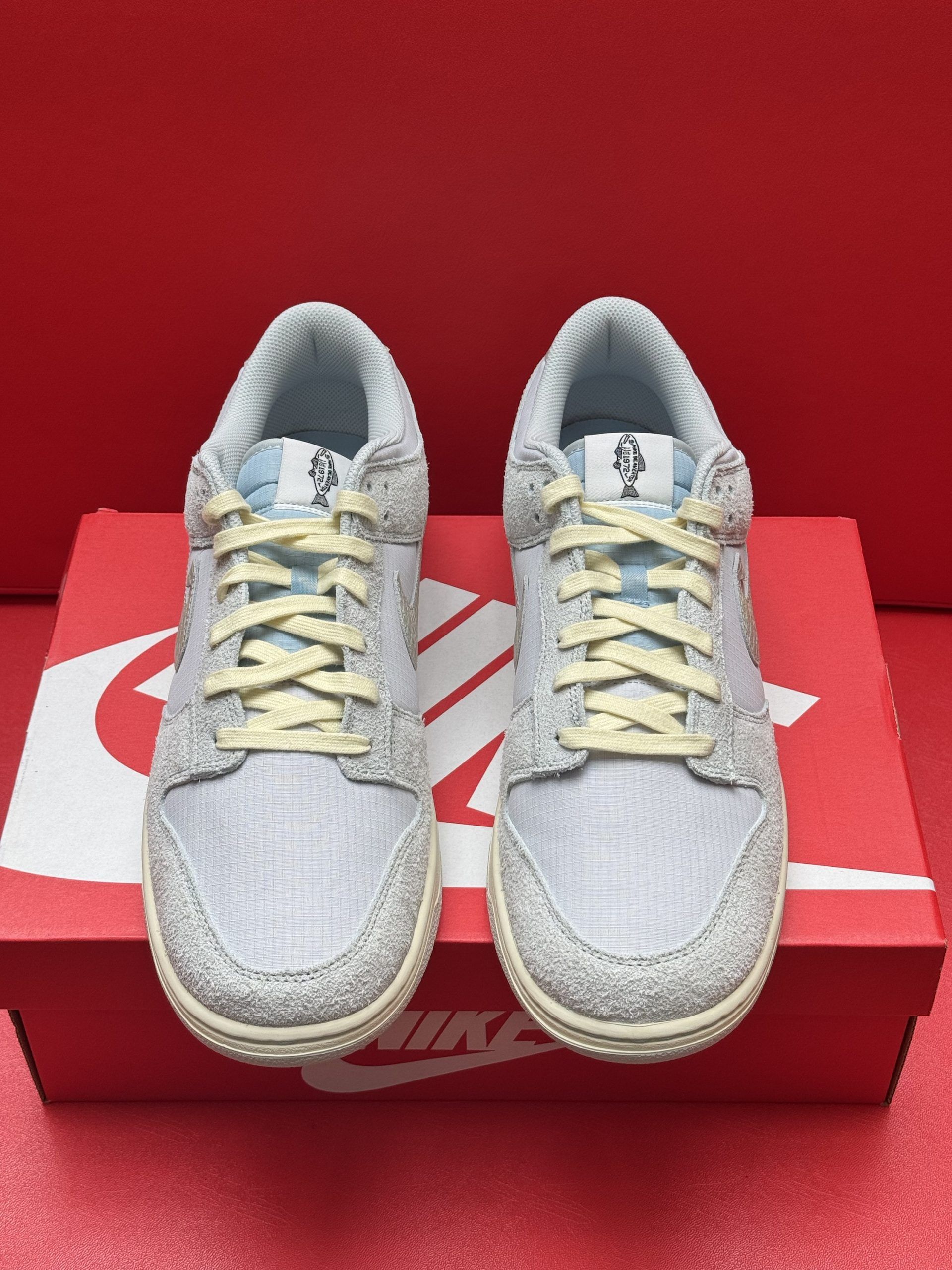 Light blue Nike Dunk Low sneakers, one atop the box, the other showing the sole. Cream laces and accents. Red box.