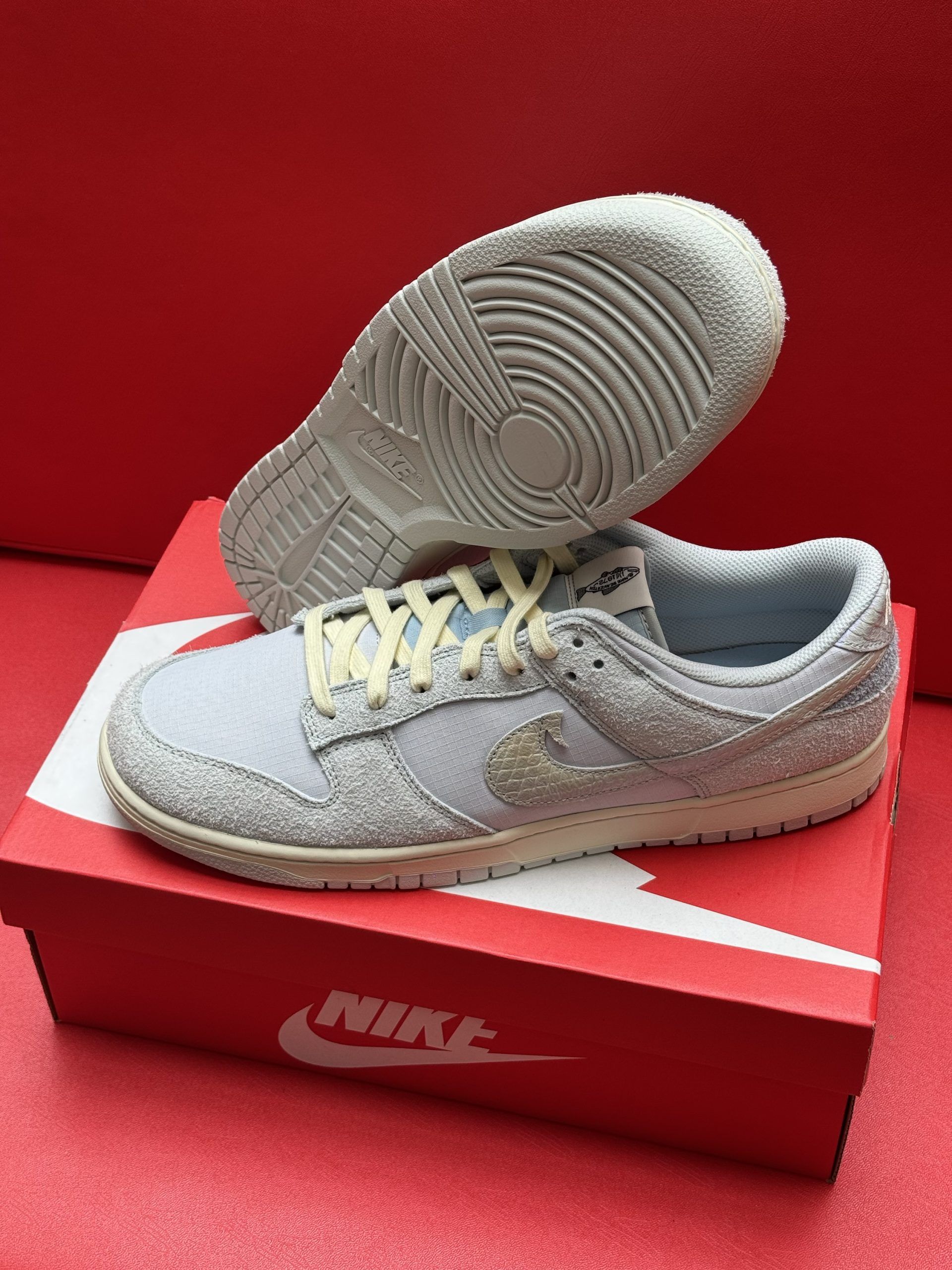 Light blue Nike Dunk Low sneakers, one atop the box, the other showing the sole. Cream laces and accents. Red box.