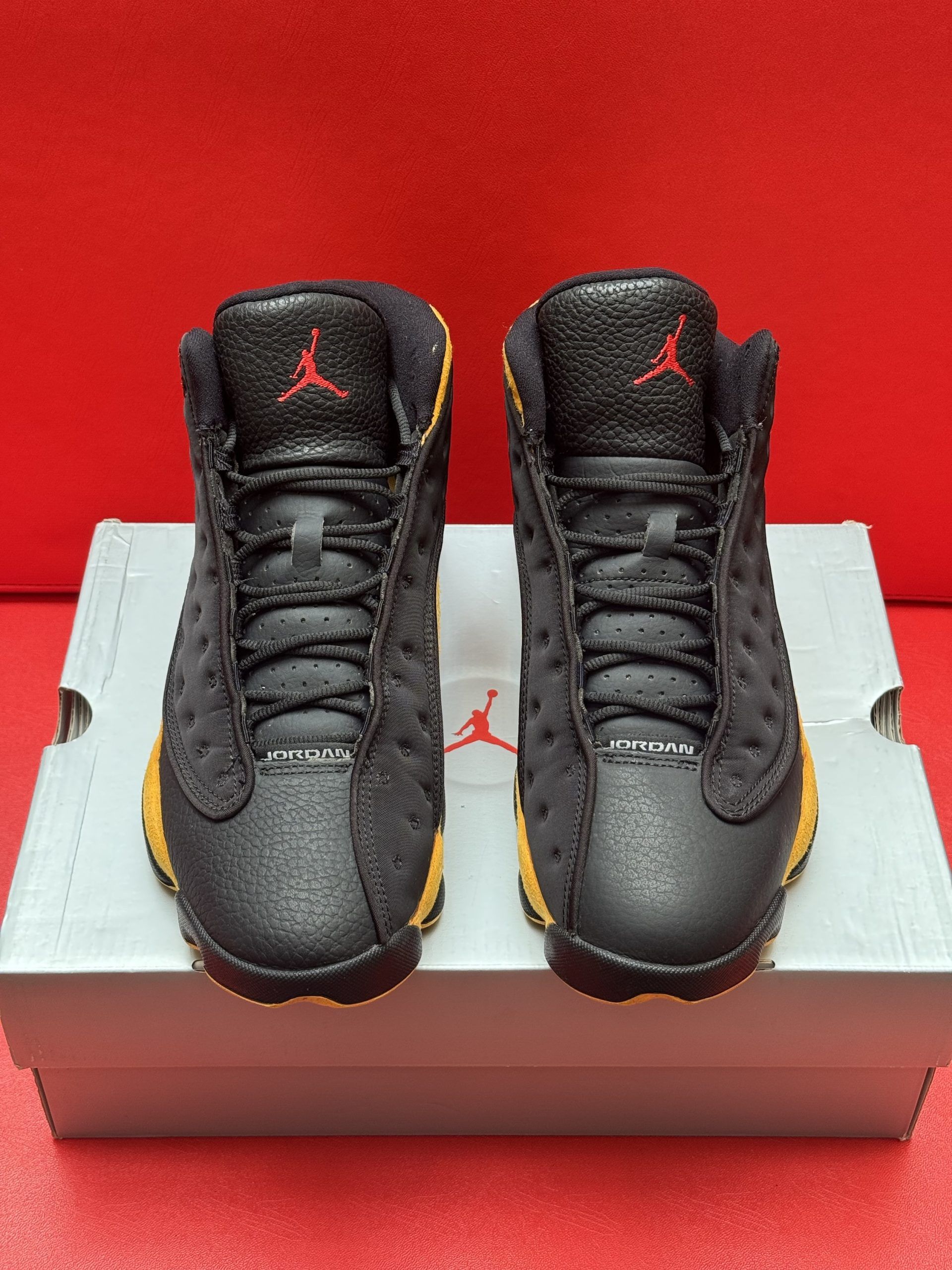 Black and yellow Air Jordan 13 sneakers on a shoebox. Red soles and a red Jumpman logo.