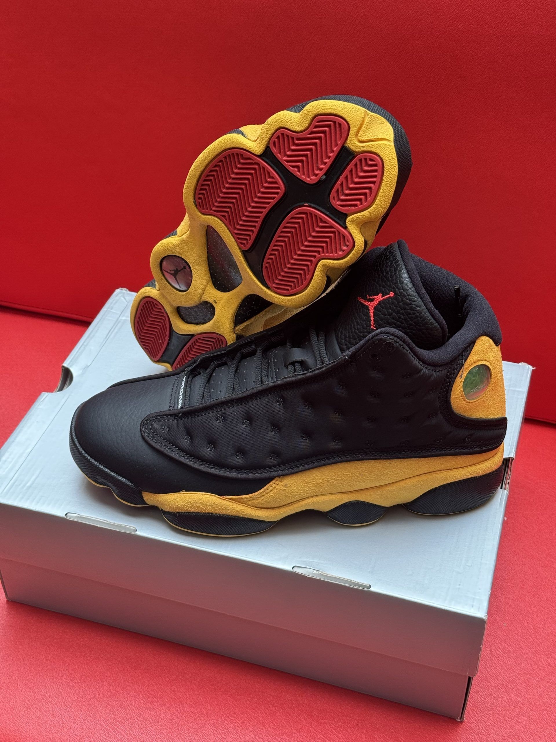 Black and yellow Air Jordan 13 sneakers on a shoebox. Red soles and a red Jumpman logo.