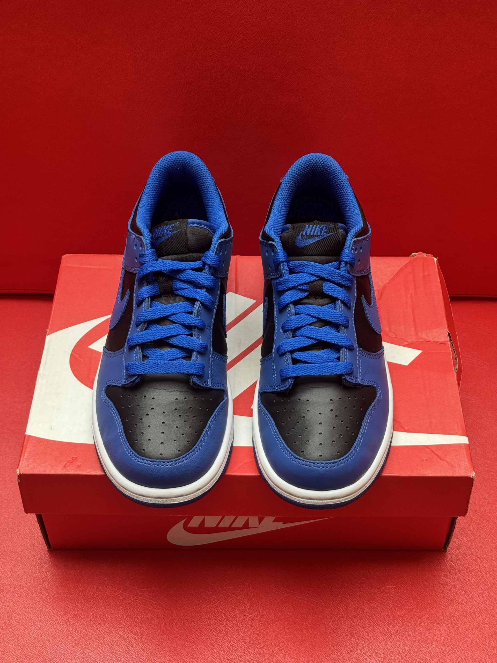 Blue and black Nike Dunk low sneakers on a red Nike box, against a red background.