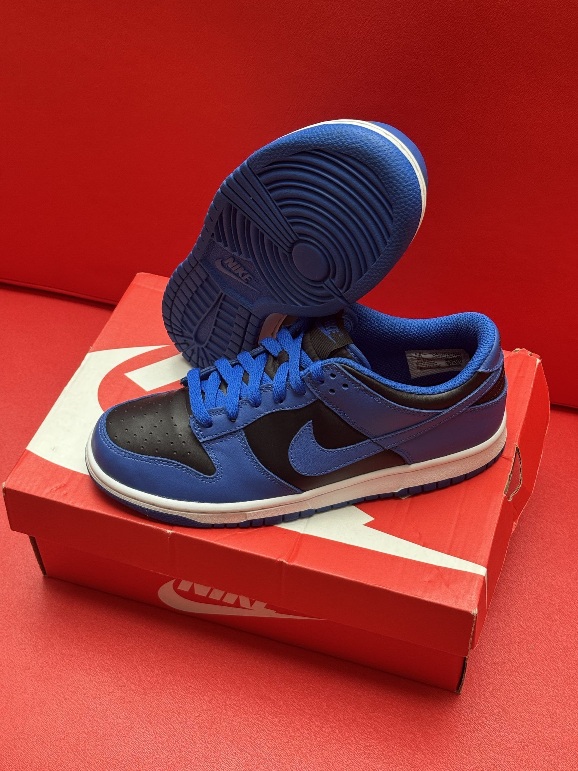 Blue and black Nike Dunk low sneakers on a red Nike box, against a red background.