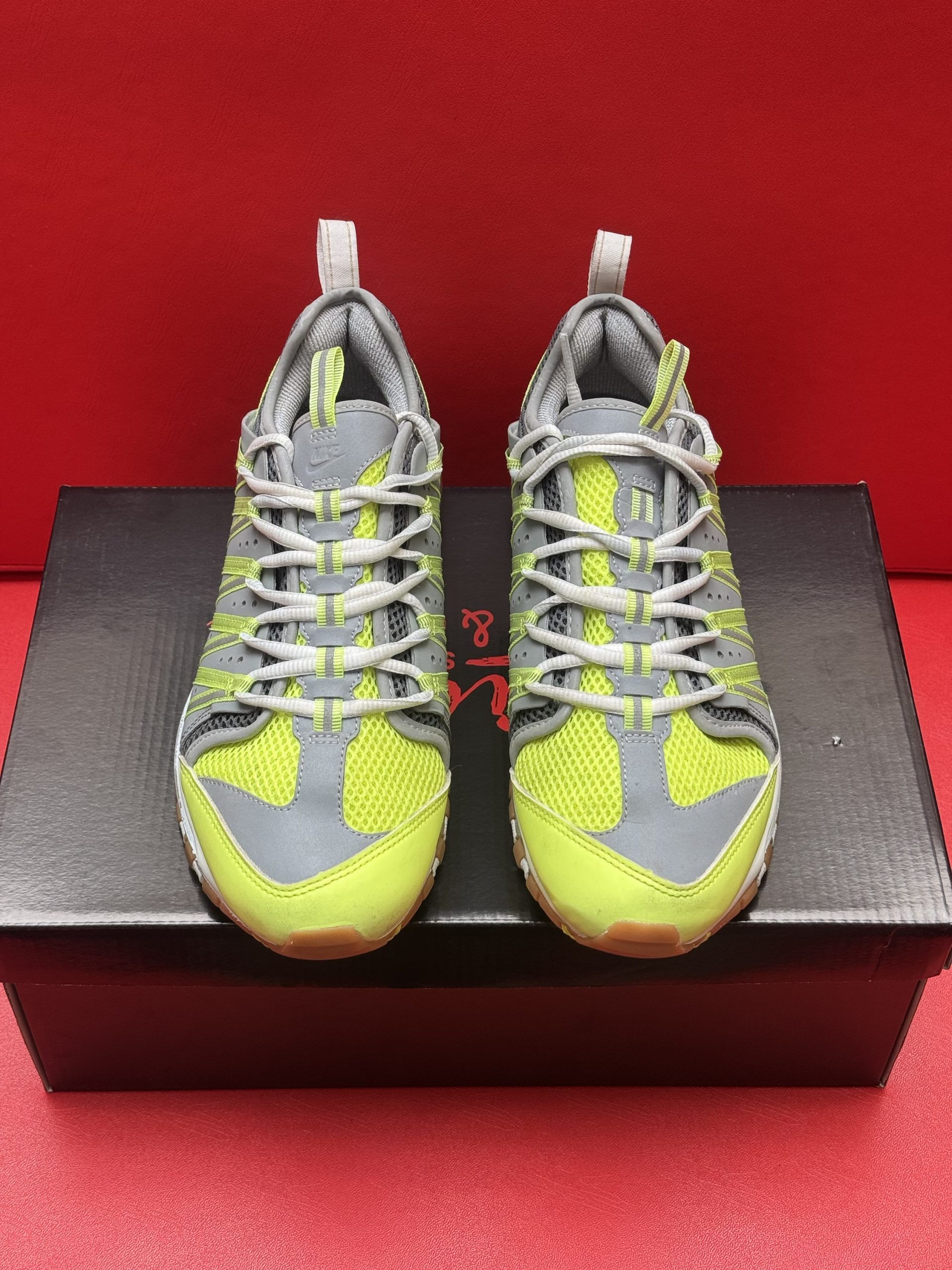 Grey and yellow athletic shoes with white laces, on top of a black box, with the sole of a shoe showing.