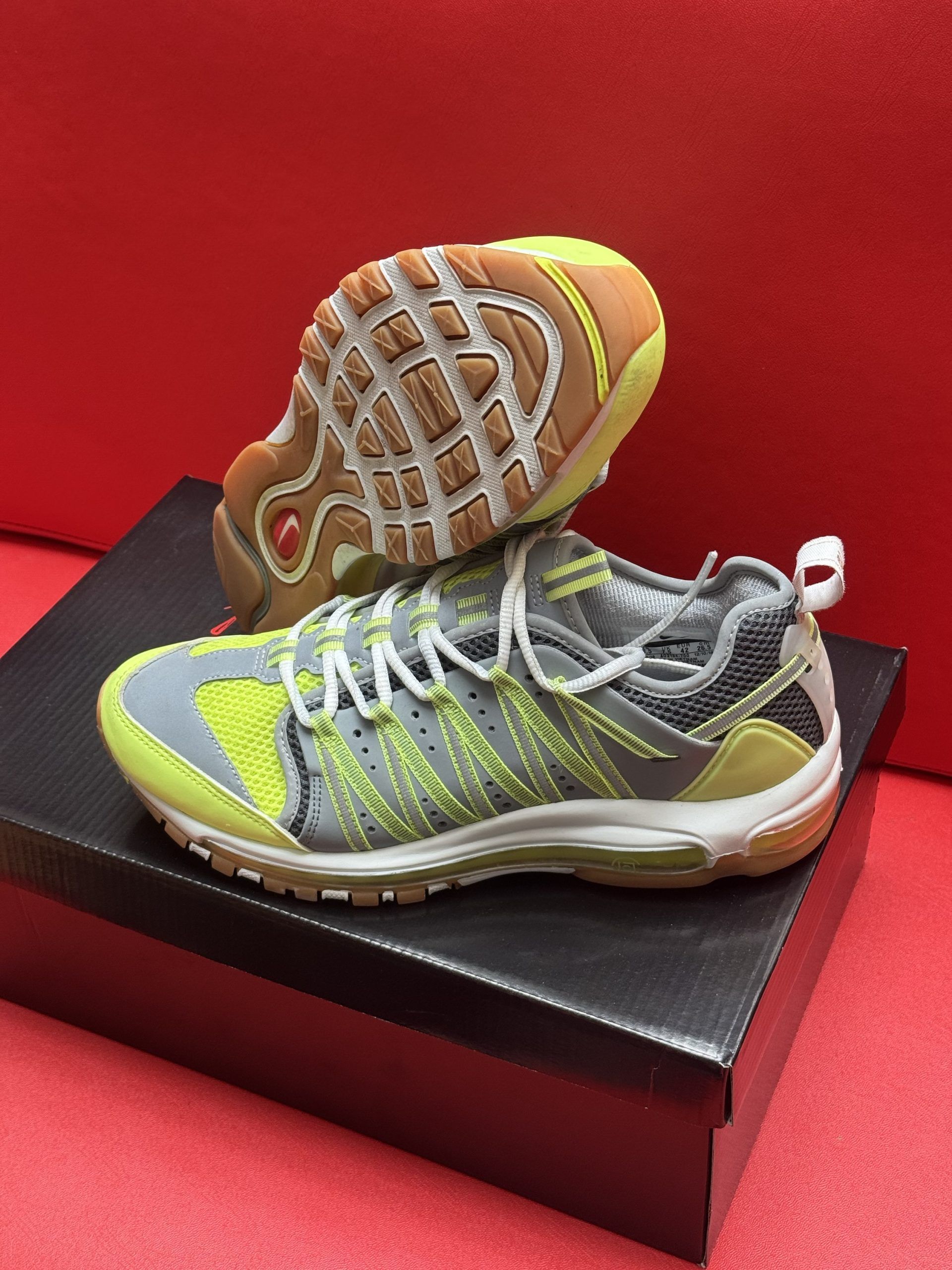 Grey and yellow athletic shoes with white laces, on top of a black box, with the sole of a shoe showing.