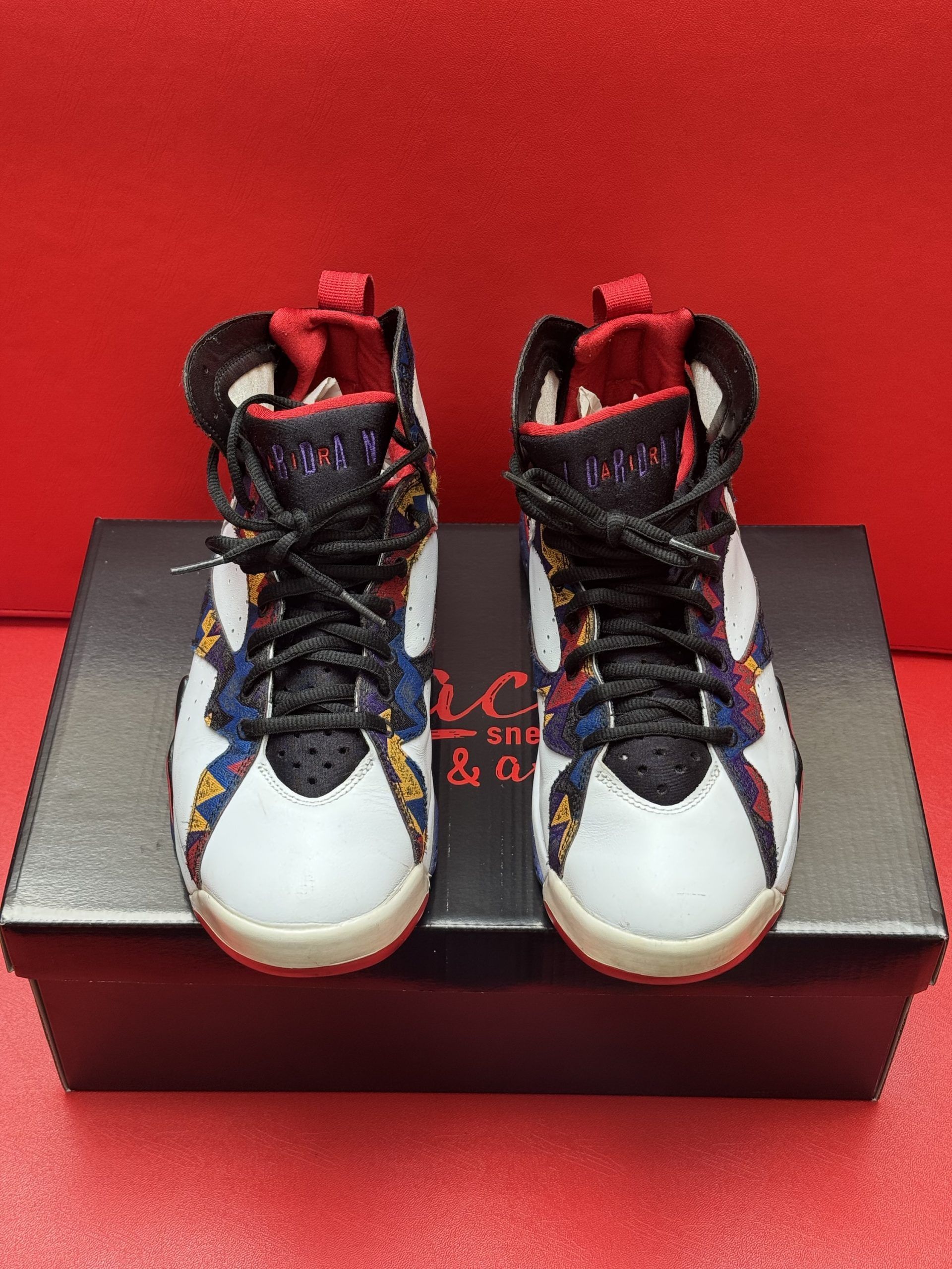 Air Jordan 7 sneakers on a black box, white, black, red, and colorful accents.