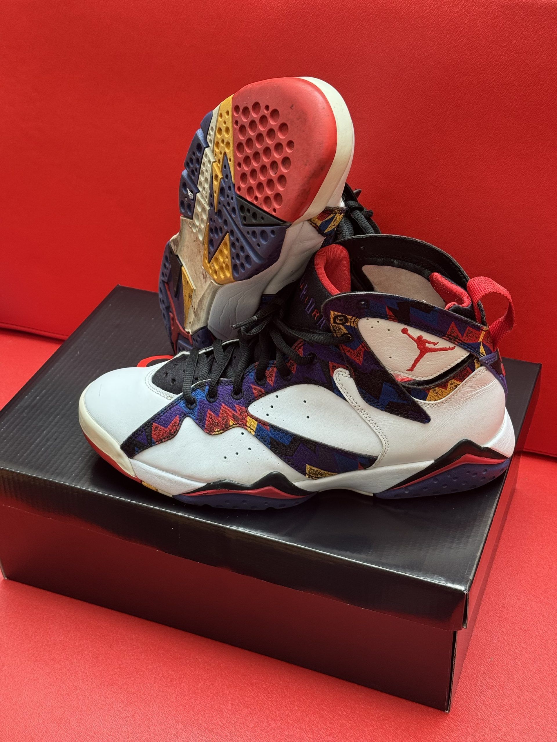Air Jordan 7 sneakers on a black box, white, black, red, and colorful accents.