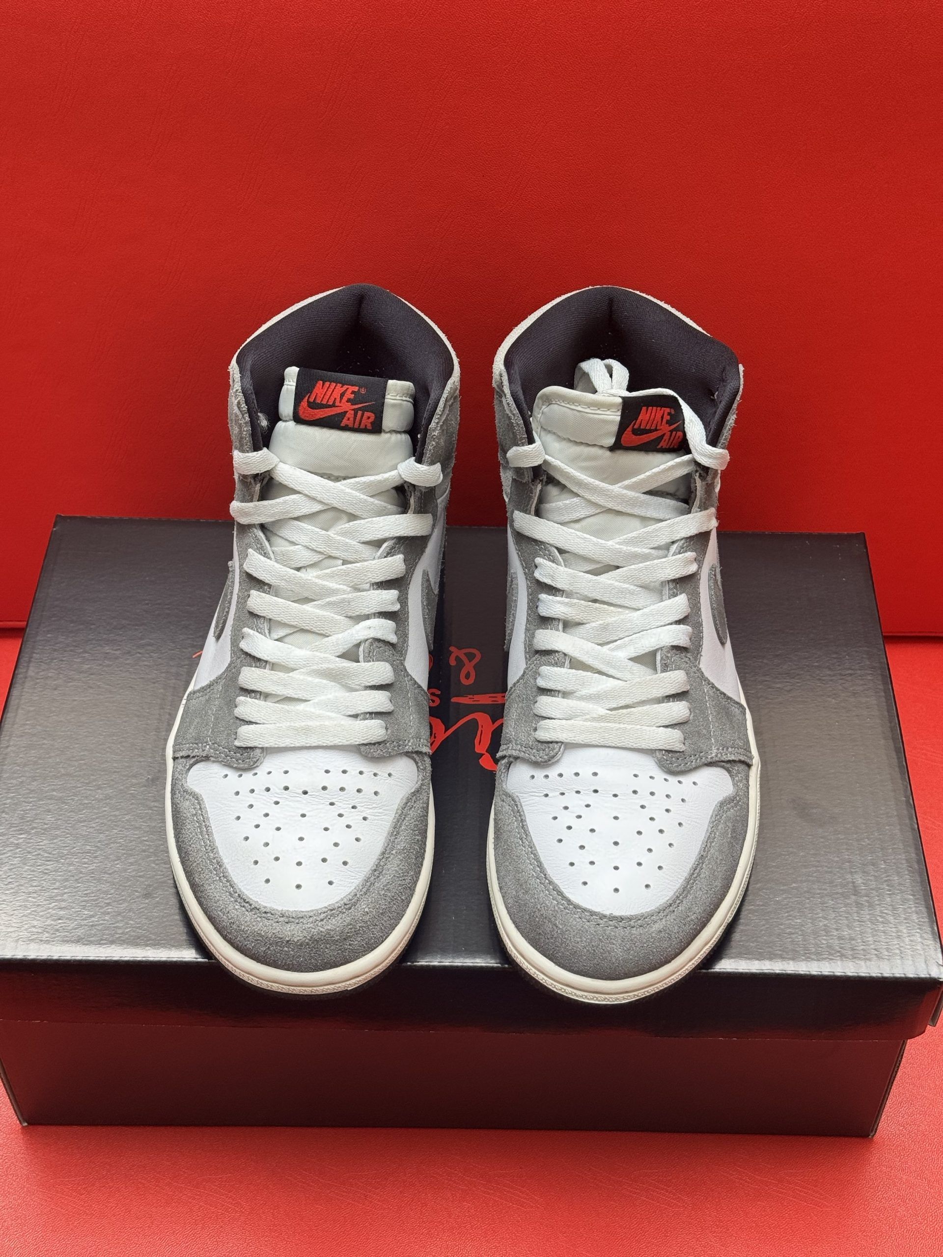 Gray and white Air Jordan 1 high-top sneakers on a black shoe box, set against a red background.